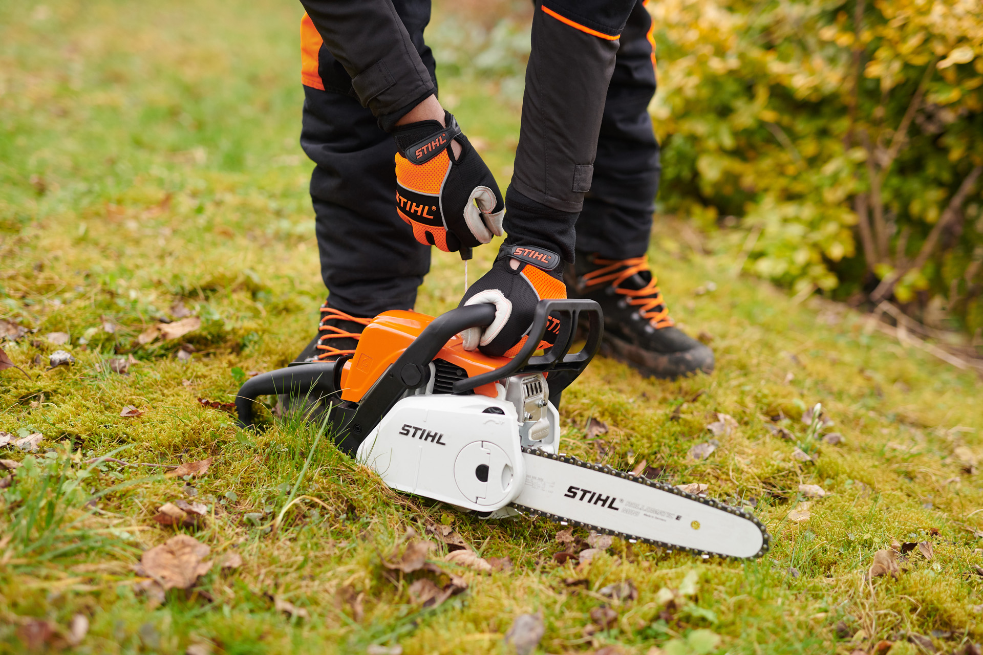 A STIHL MS 180 C-BE petrol chainsaw with ErgoStart on grass, being started up