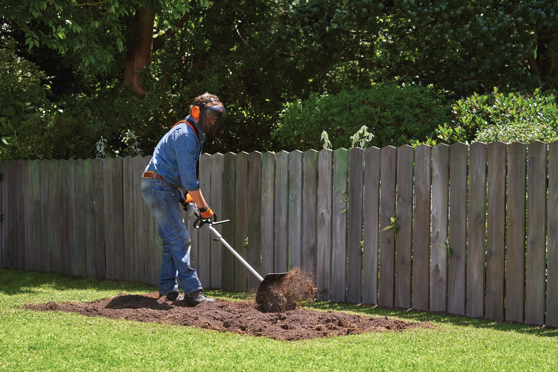 A person wearing personal protective equipment cultivates soil for a vegetable bed using a STIHL KombiSystem with pick tine