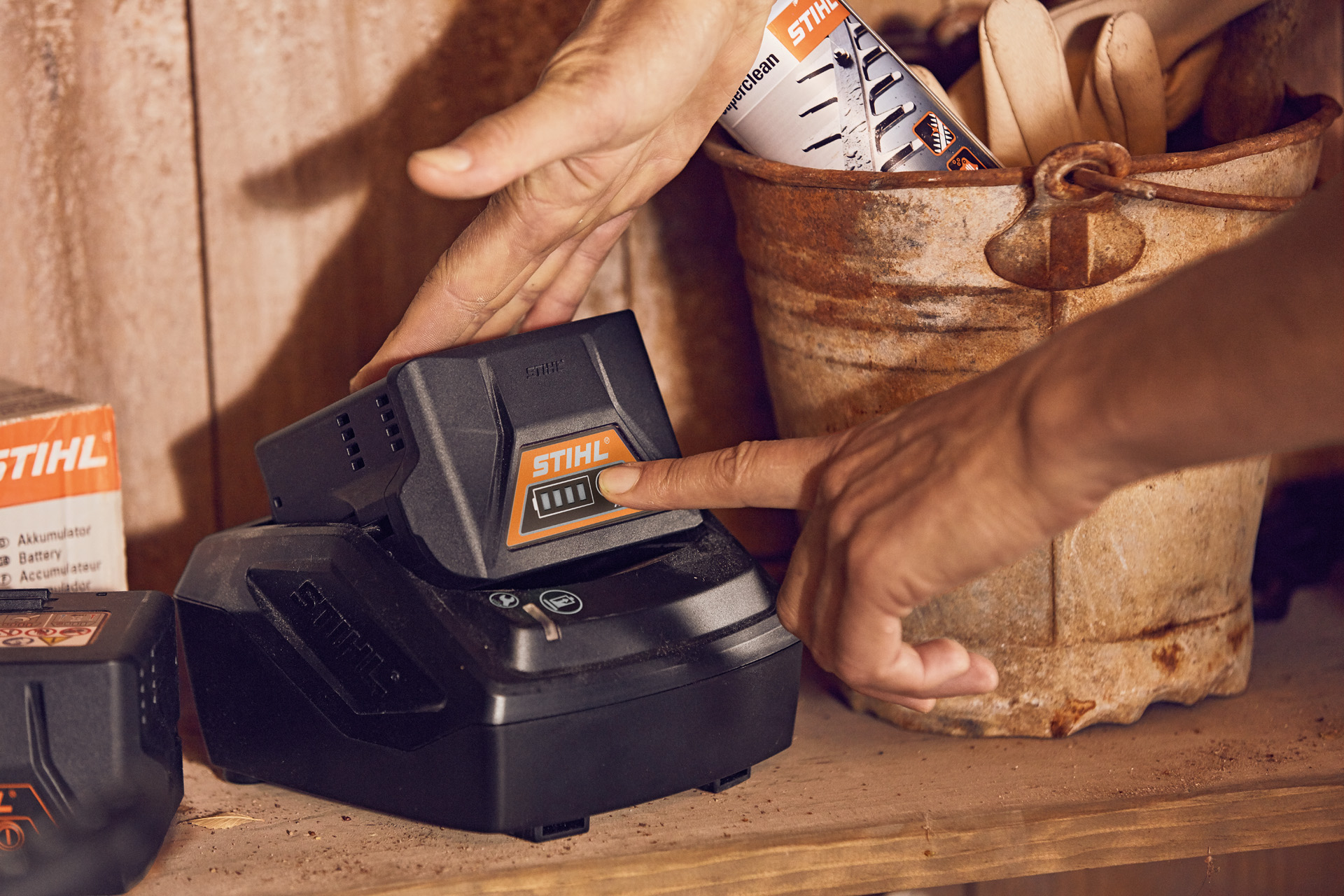 A STIHL AK 10 battery in a charger on a shelf, as someone checks the power level