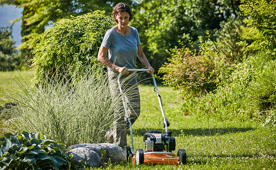 Woman mows lawn in her garden in summer with STIHL mulching lawn mower RM 2 R