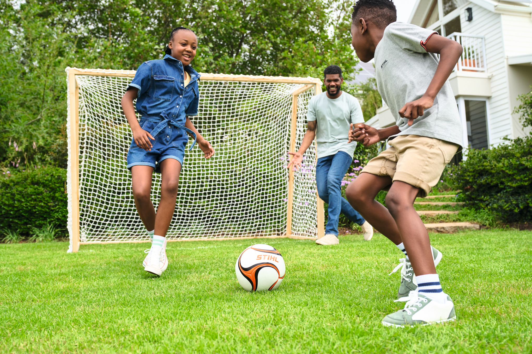 Three children playing football with a wooden football goal in the garden