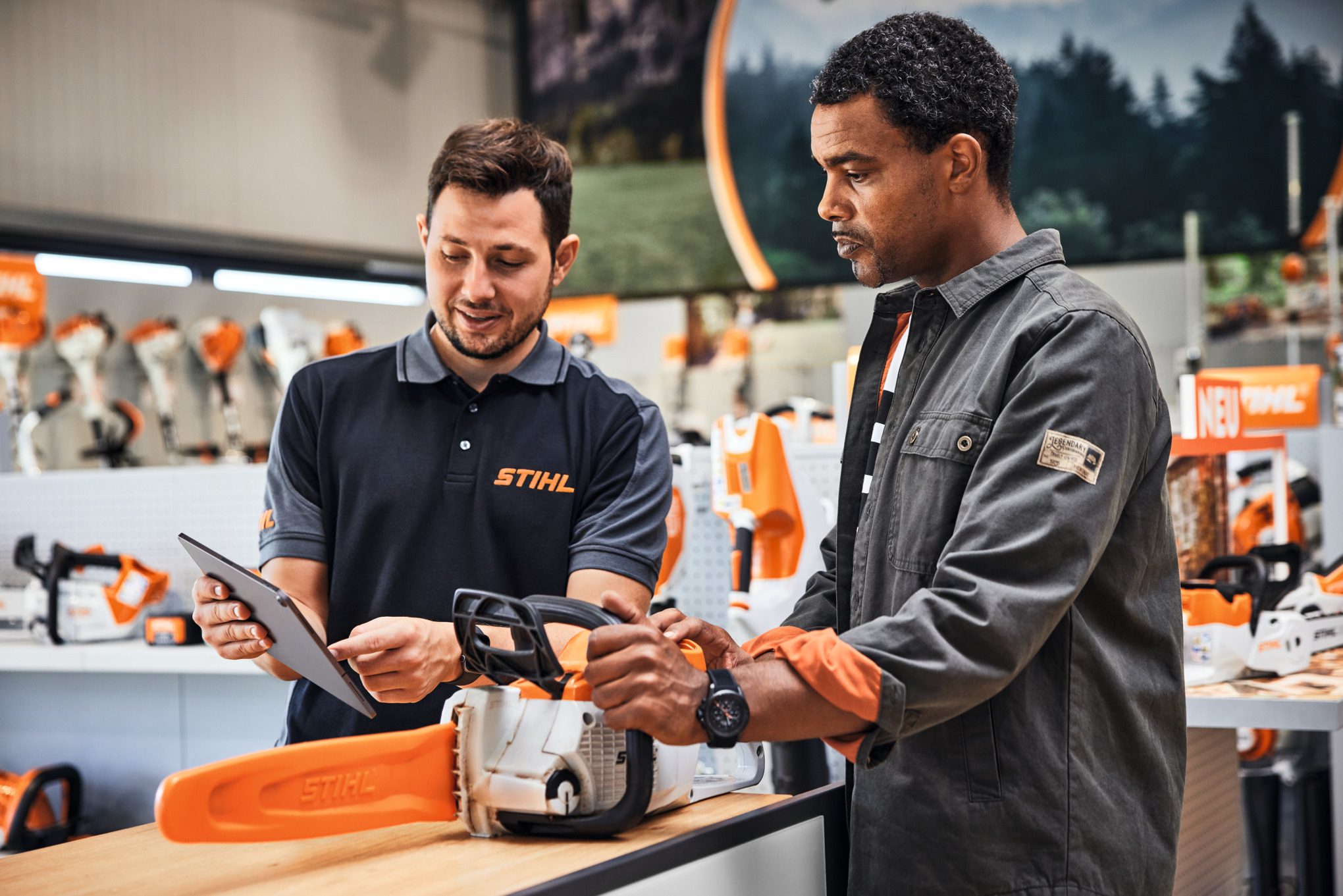 Two men speak at a counter about a STIHL chainsaw