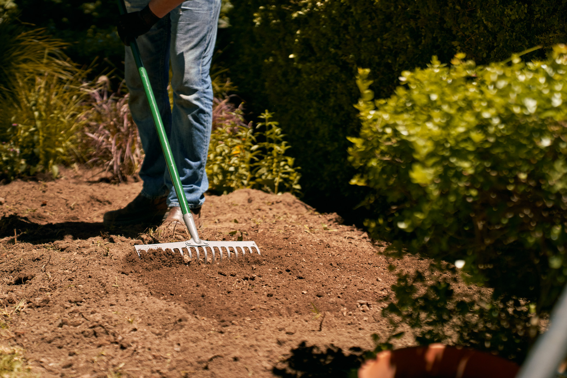 A person using a rake to level soil in a garden bed