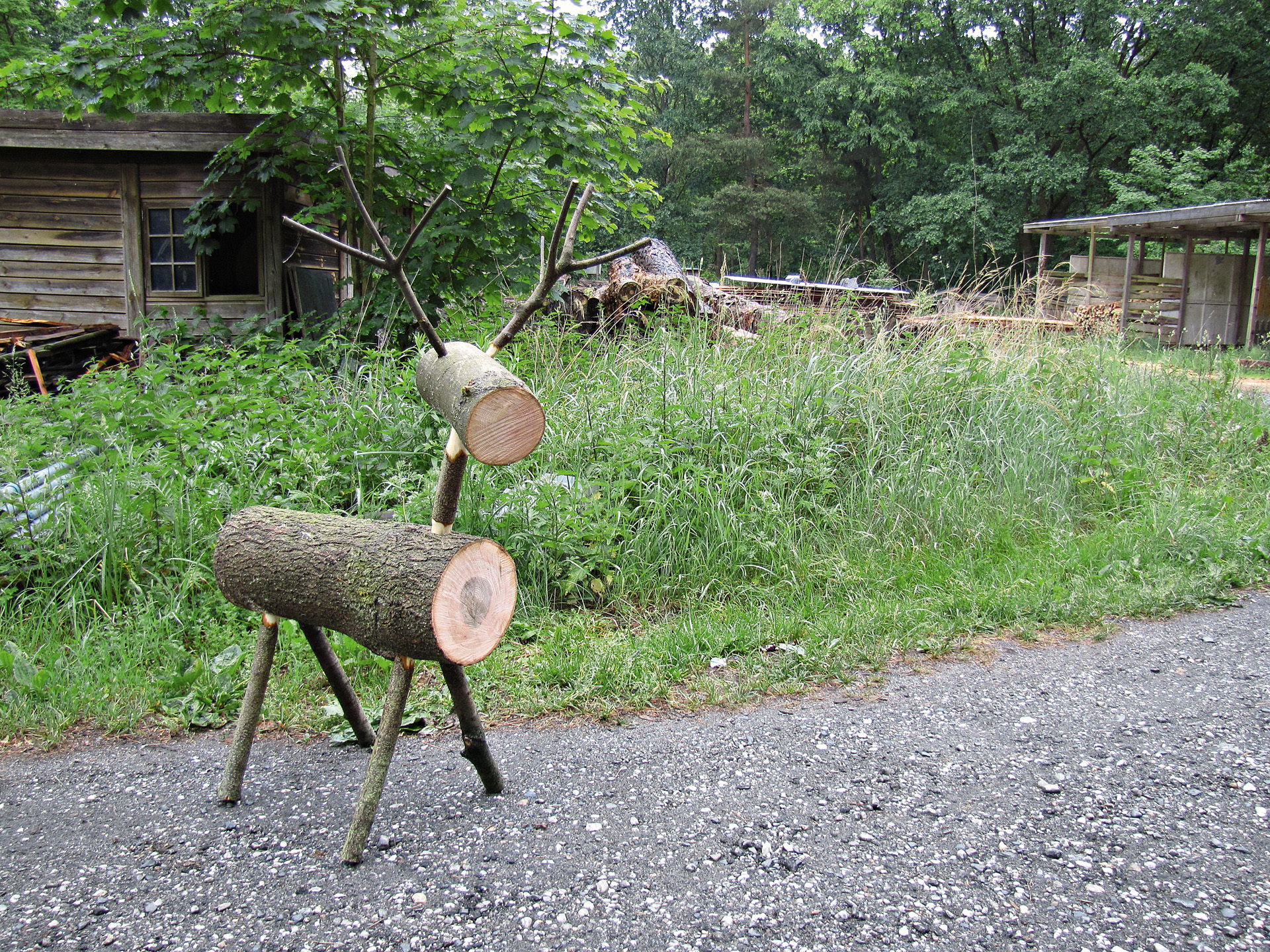 DIY log reindeer in front of green grass and shed