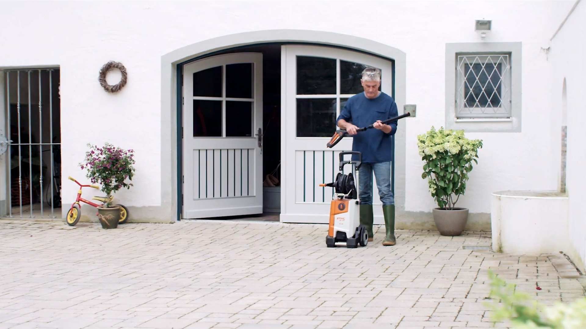 A man standing in front of a white house, preparing to clean the exterior with a STIHL pressure washer