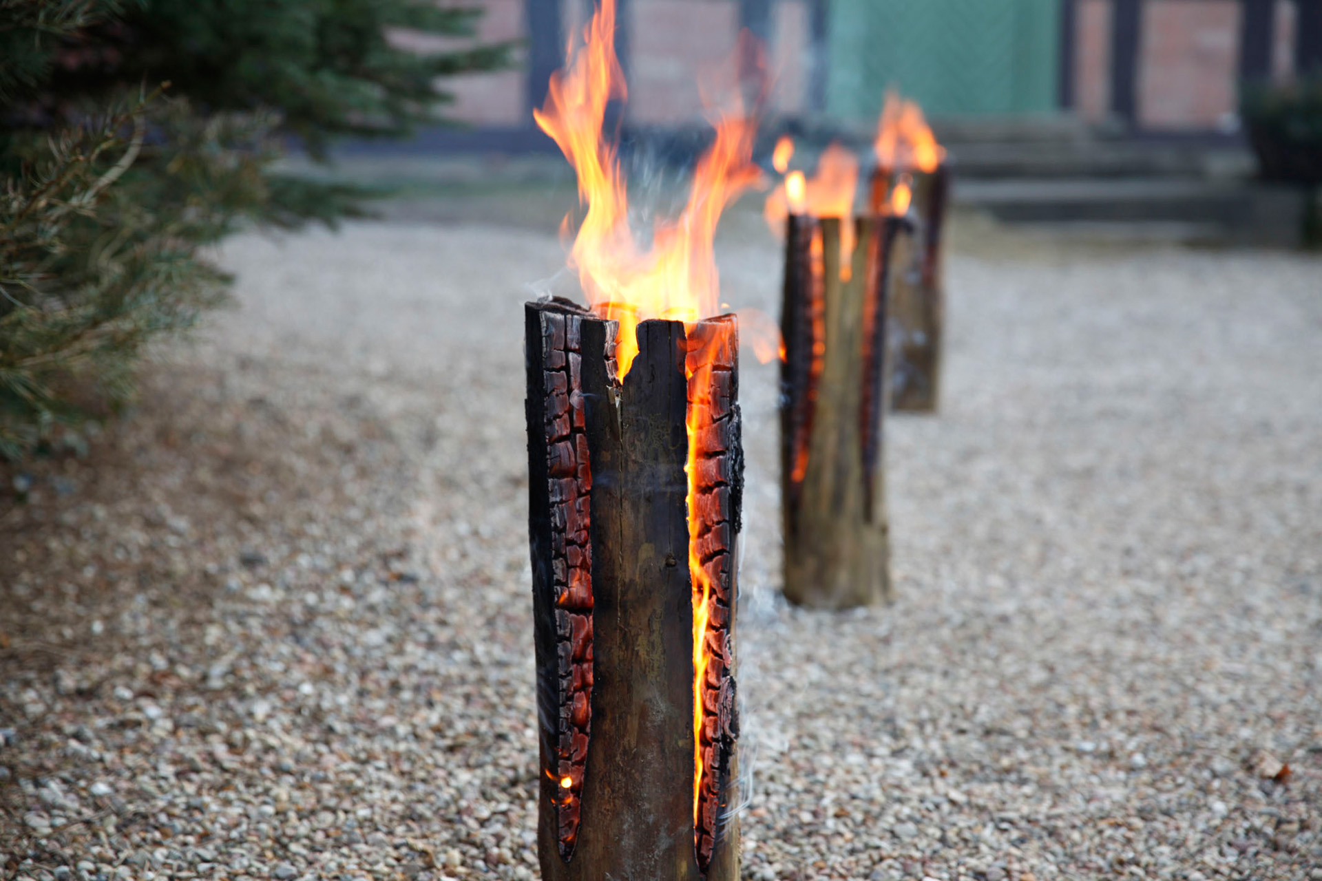 Three burning DIY Swedish fire logs set up on a gravel path