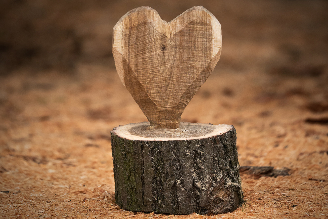 A finished DIY carved-wood heart sculpture surrounded by wood shavings