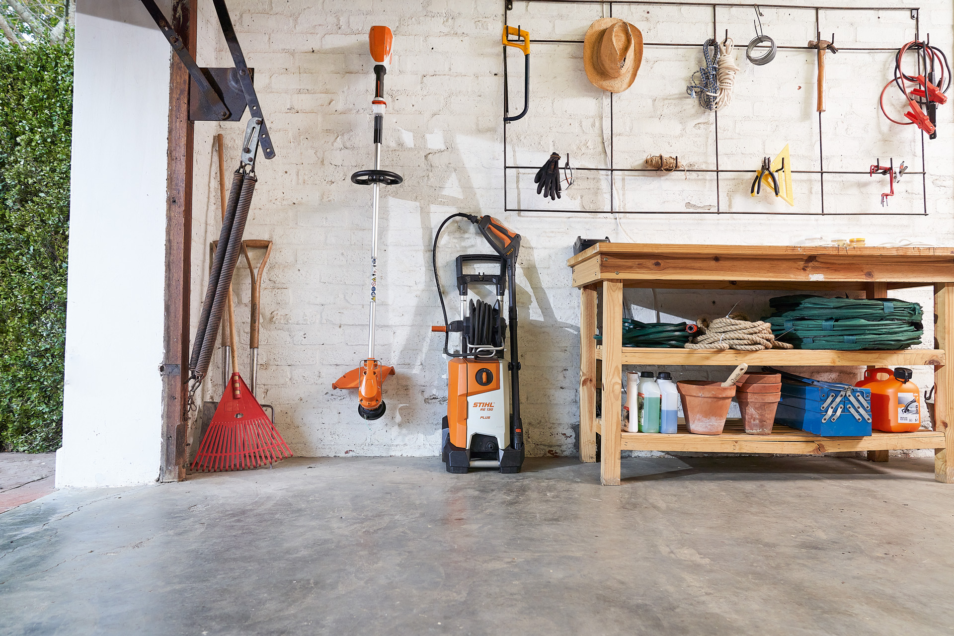 A STIHL RE 130 plus high-pressure cleaner and a STIHL brushcutter stored next to garden tools in a garage 