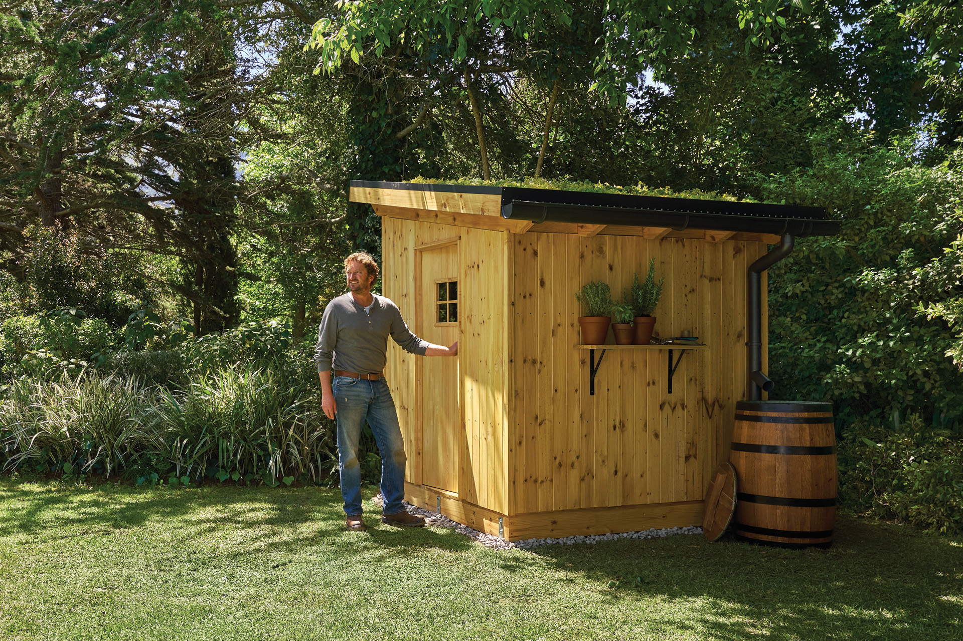 A man standing beside a finished garden shed with trees behind it