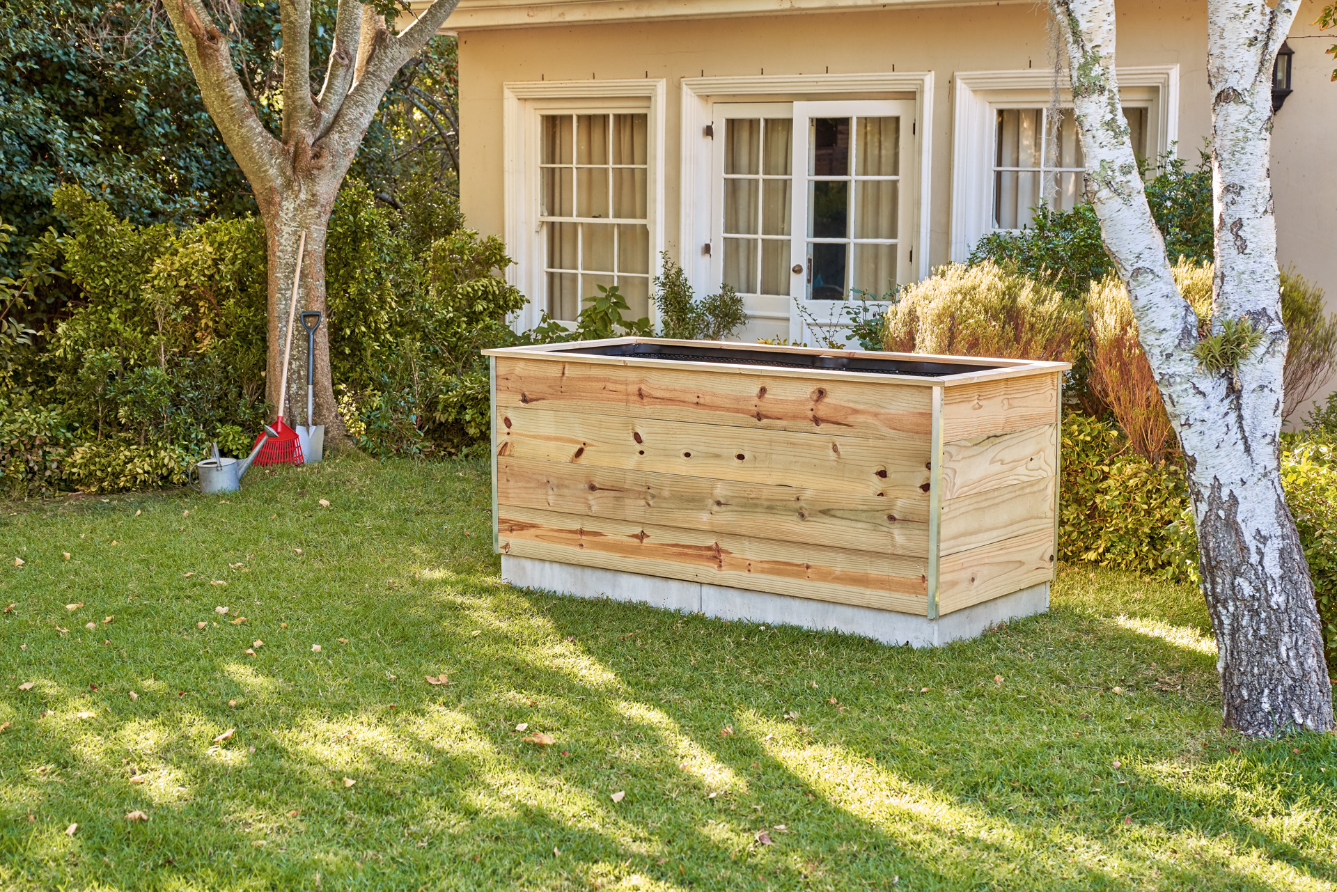 A tall raised bed made from wooden boards, in the garden in front of a house.