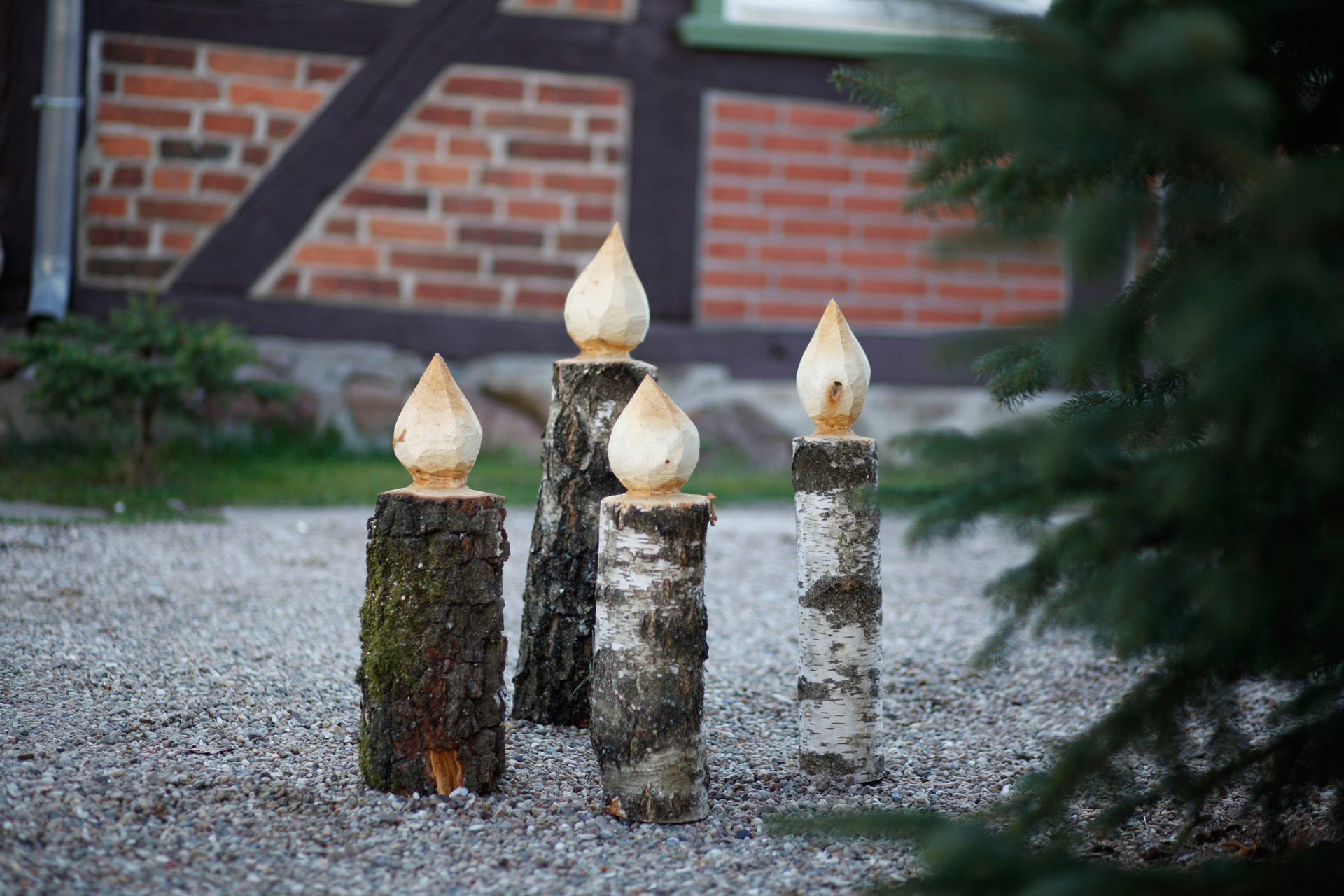 Four DIY wooden candlesticks standing on a path beside a fir tree