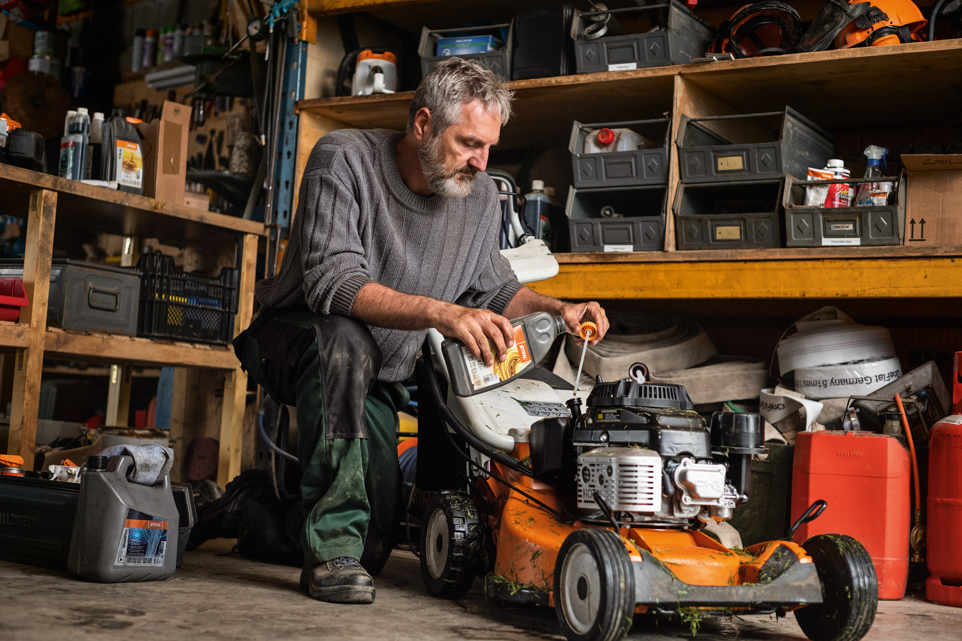 A man performing maintenance work on a STIHL RM 756 petrol lawn mower in the garage