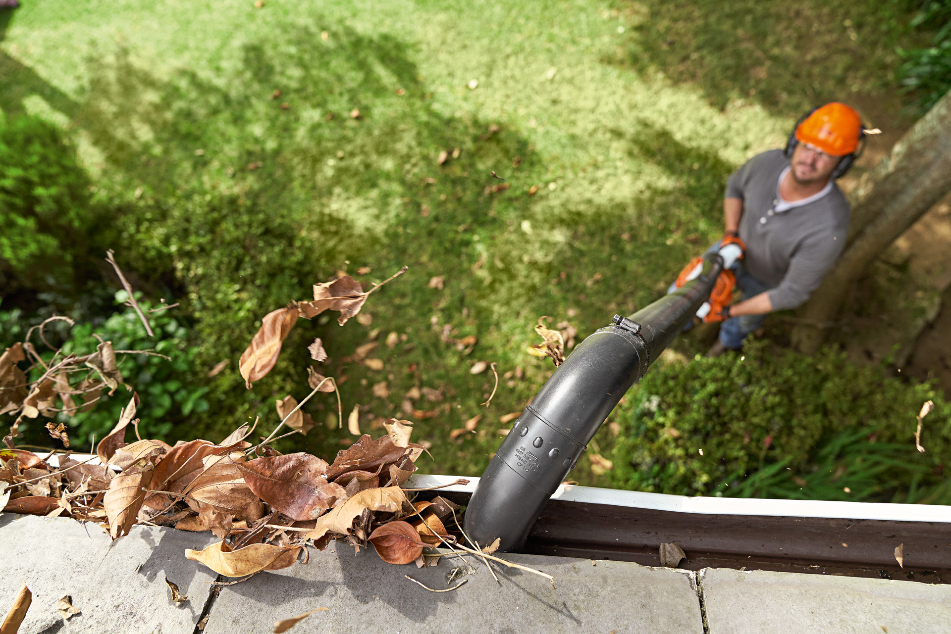 Overhead shot of a gutter full of leaves being cleaned by a man  with a STIHL leaf blower and gutter cleaning set