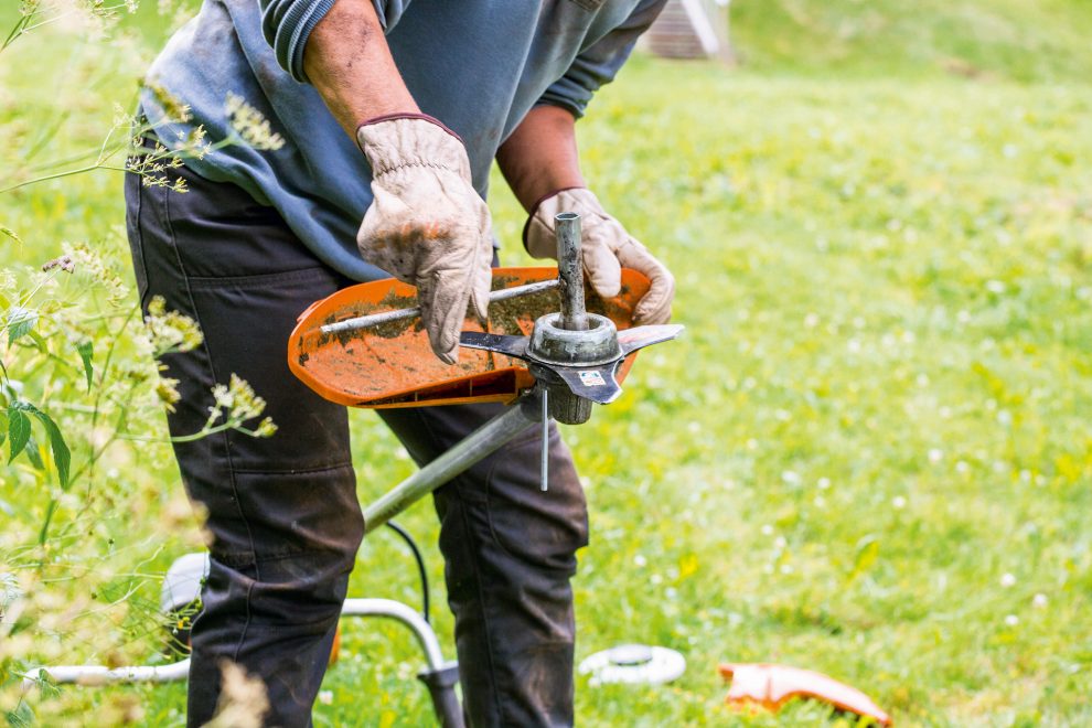 A man wearing gloves cleans the cutting tool of a STIHL FS 131 brushcutter
