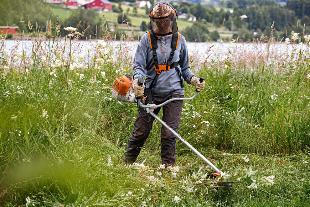 Woman using STIHL FS 240 grass trimmer with face protection beside a lake