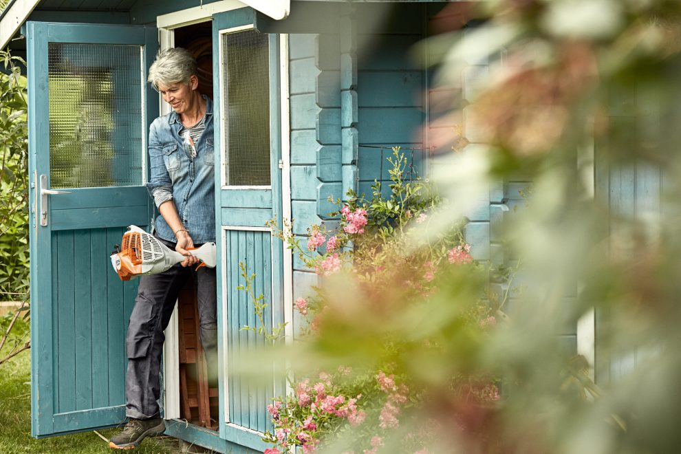 Woman coming out of a blue shed holding a STIHL FS 56 R petrol grass trimmer