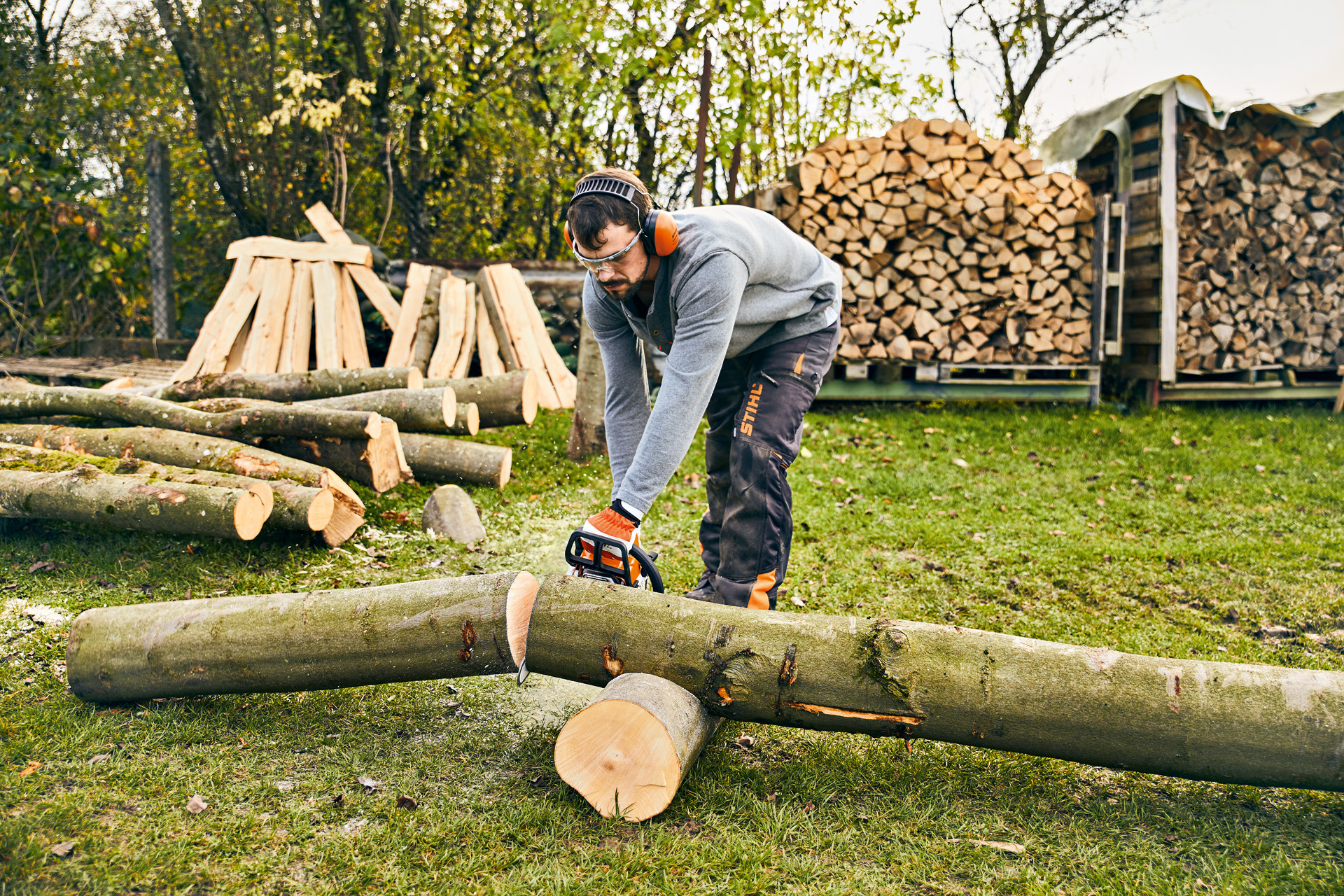 Man wearing protective goggles and ear protection sawing a log with a STIHL MS 180 petrol-driven chainsaw