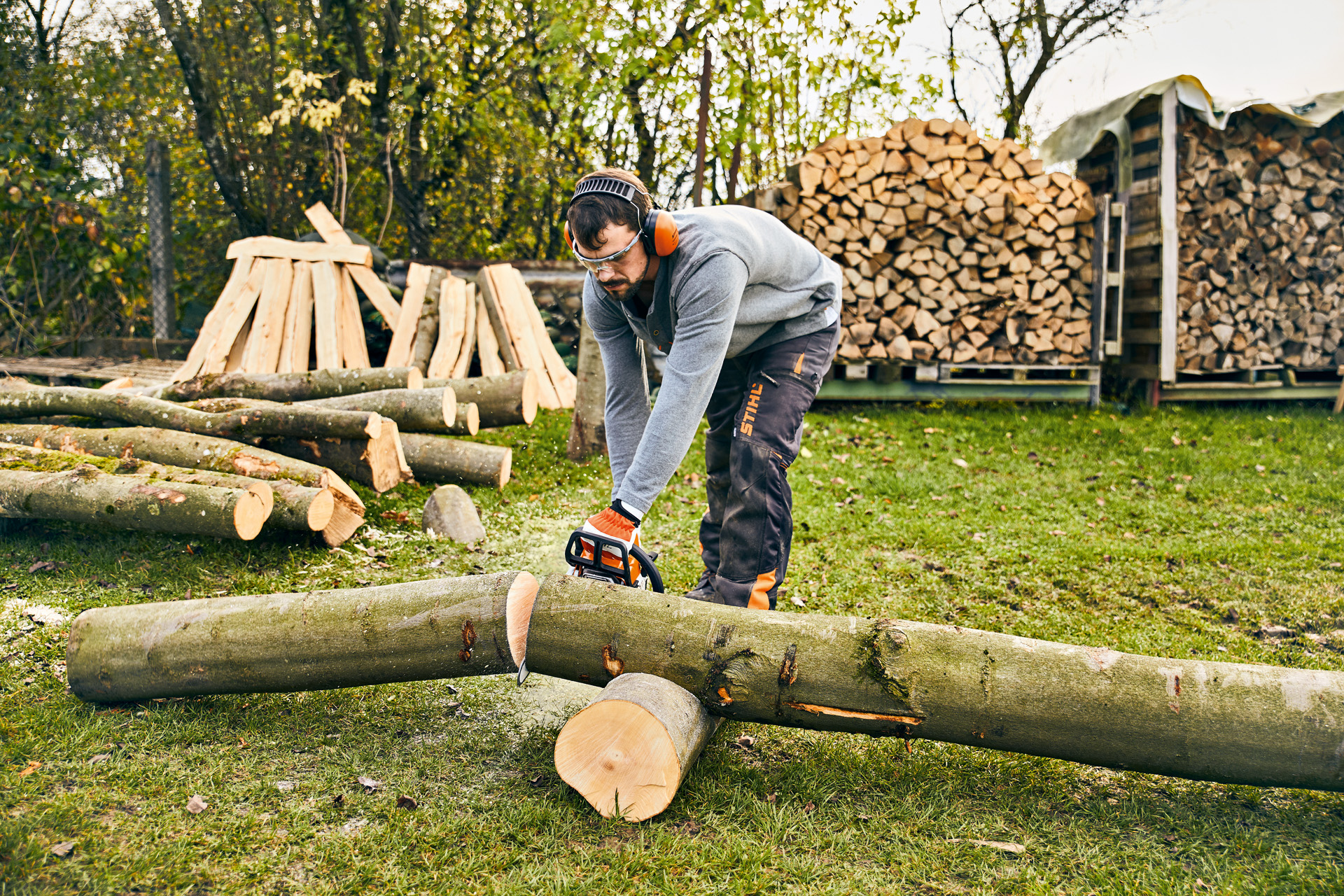 Man cutting a tree trunk with a STIHL MS 180 chain saw to build a DIY wood planter box.