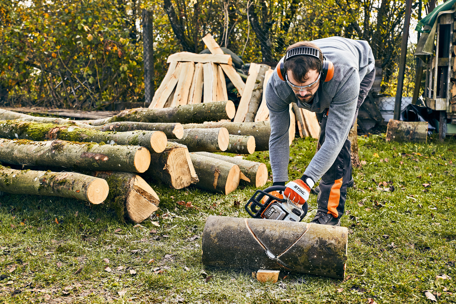 A man wearing ear protection using a STIHL MS 180 chainsaw is working on a DIY garden bench