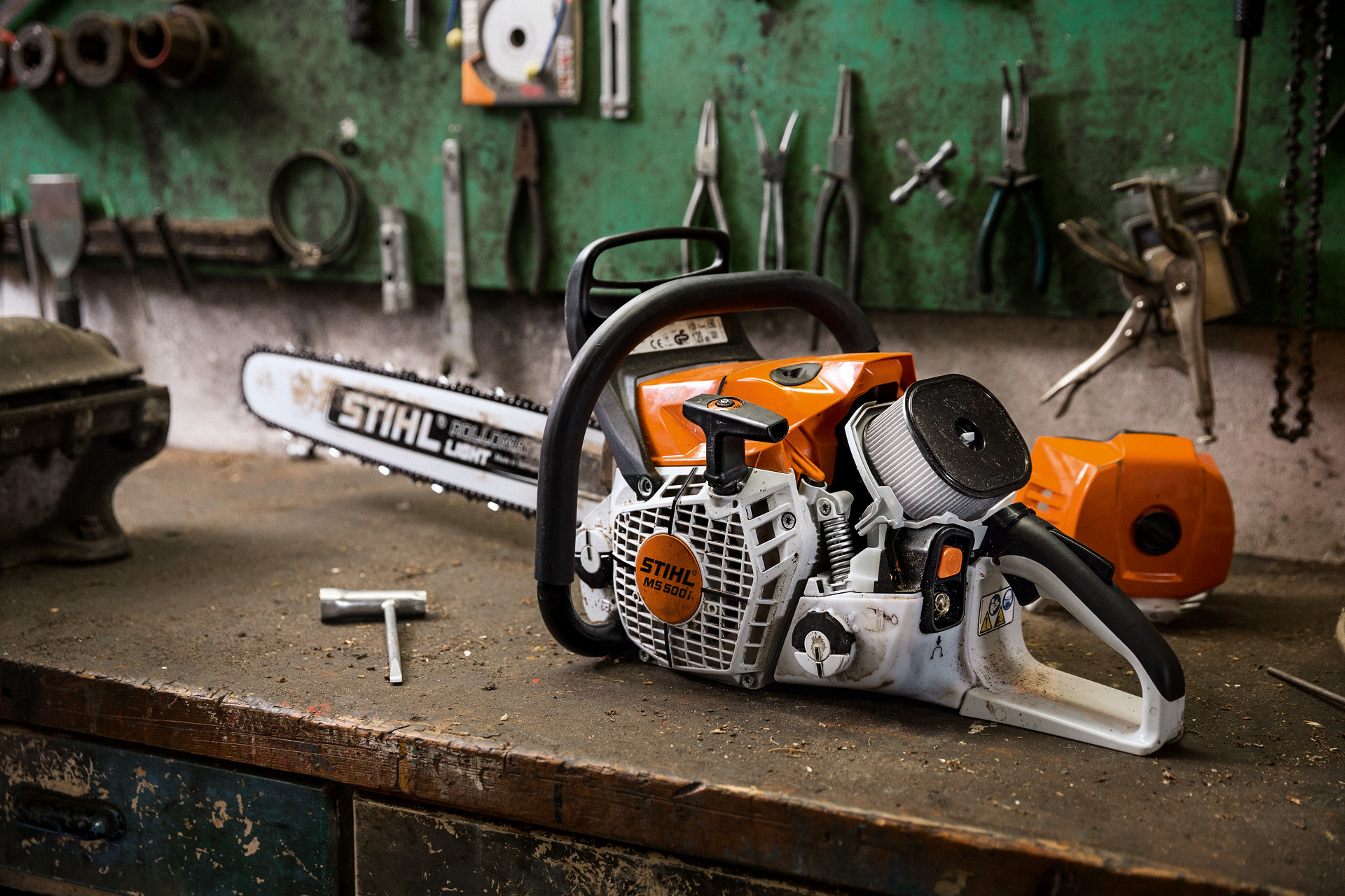 A STIHL MS 500i W petrol chainsaw on a workbench with tools hanging on the wall behind