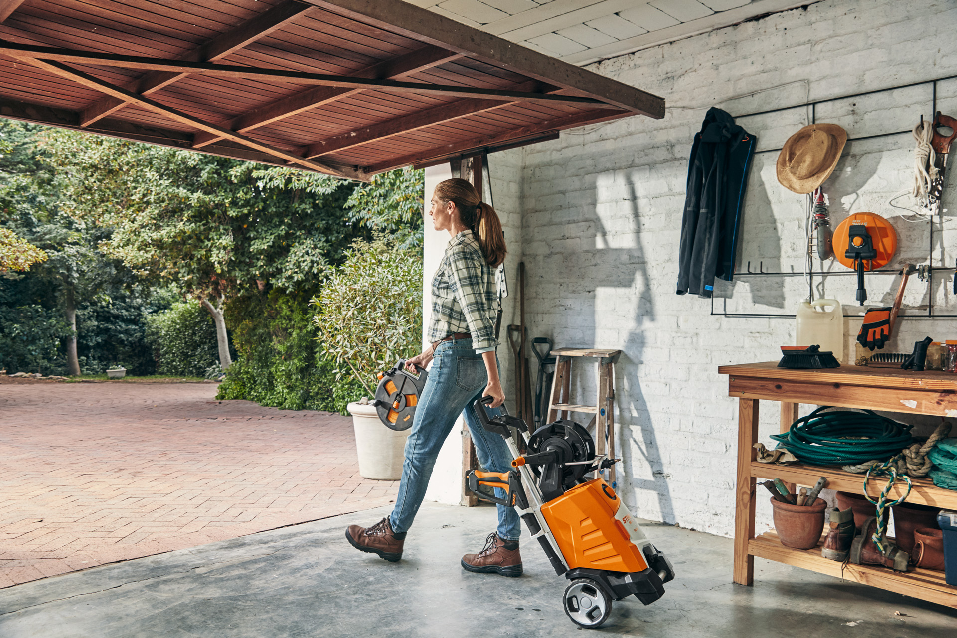 A woman exiting a garage with a STIHL RE 130 PLUS high-pressure cleaner that she is about to use