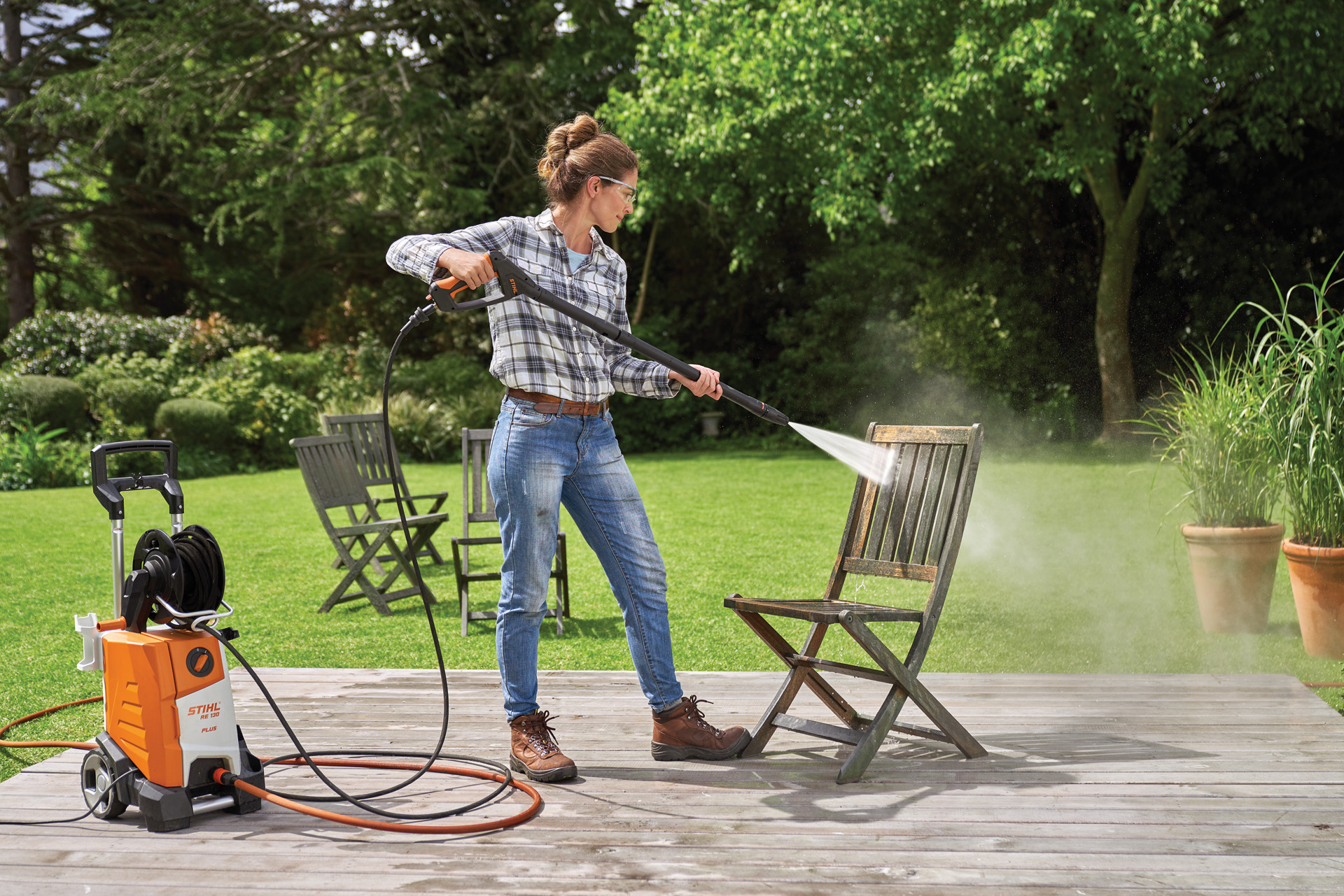 A woman using a STIHL RE 130 Plus high-pressure cleaner to clean a wooden garden chair on a patio
