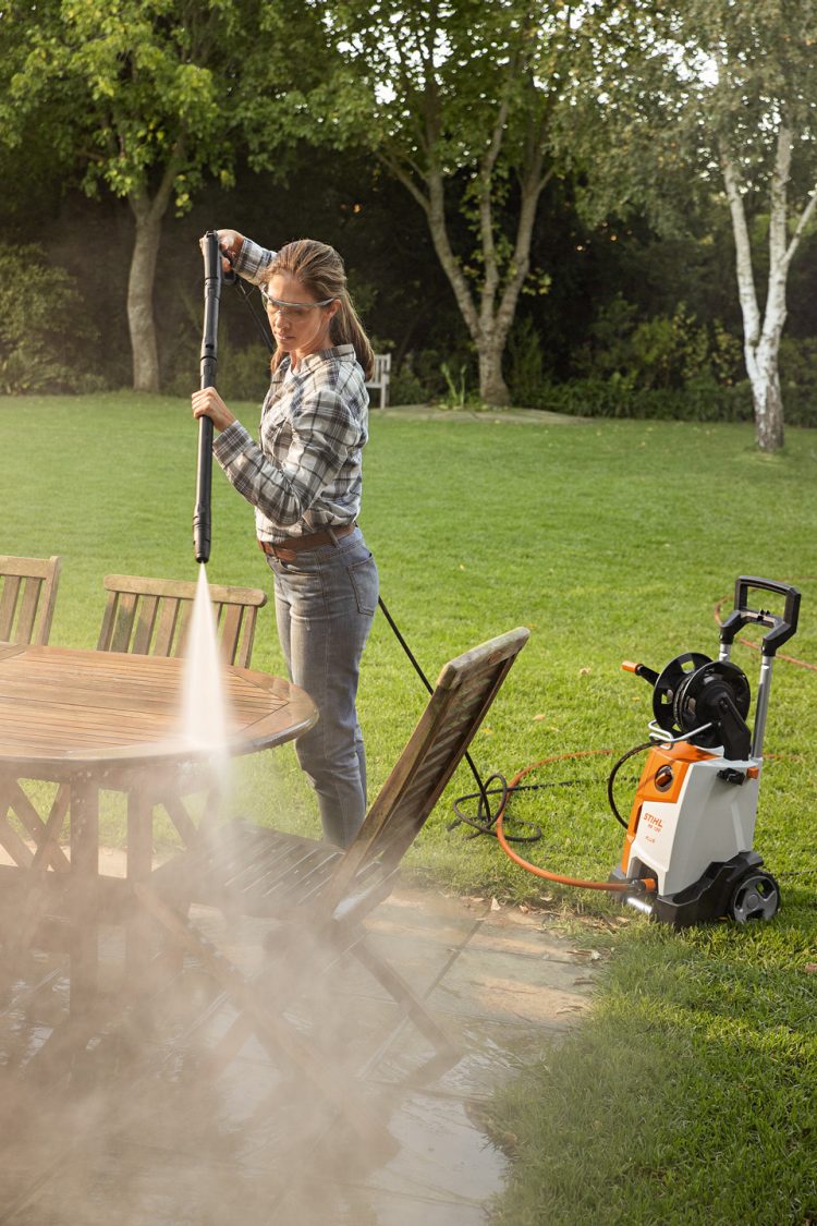 Woman using STIHL RE 130 PLUS high-pressure cleaner to clean garden furniture