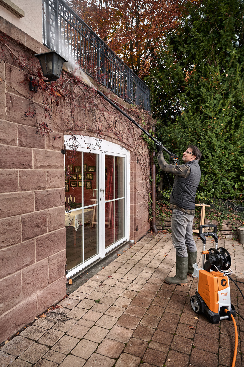 A man standing on a terrace and cleaning the exterior of a house using a STIHL pressure washer