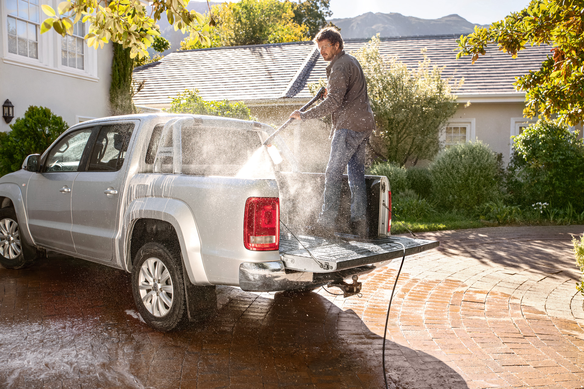 A man standing on the truck bed of a pick-up, cleaning the vehicle with a pressure washer