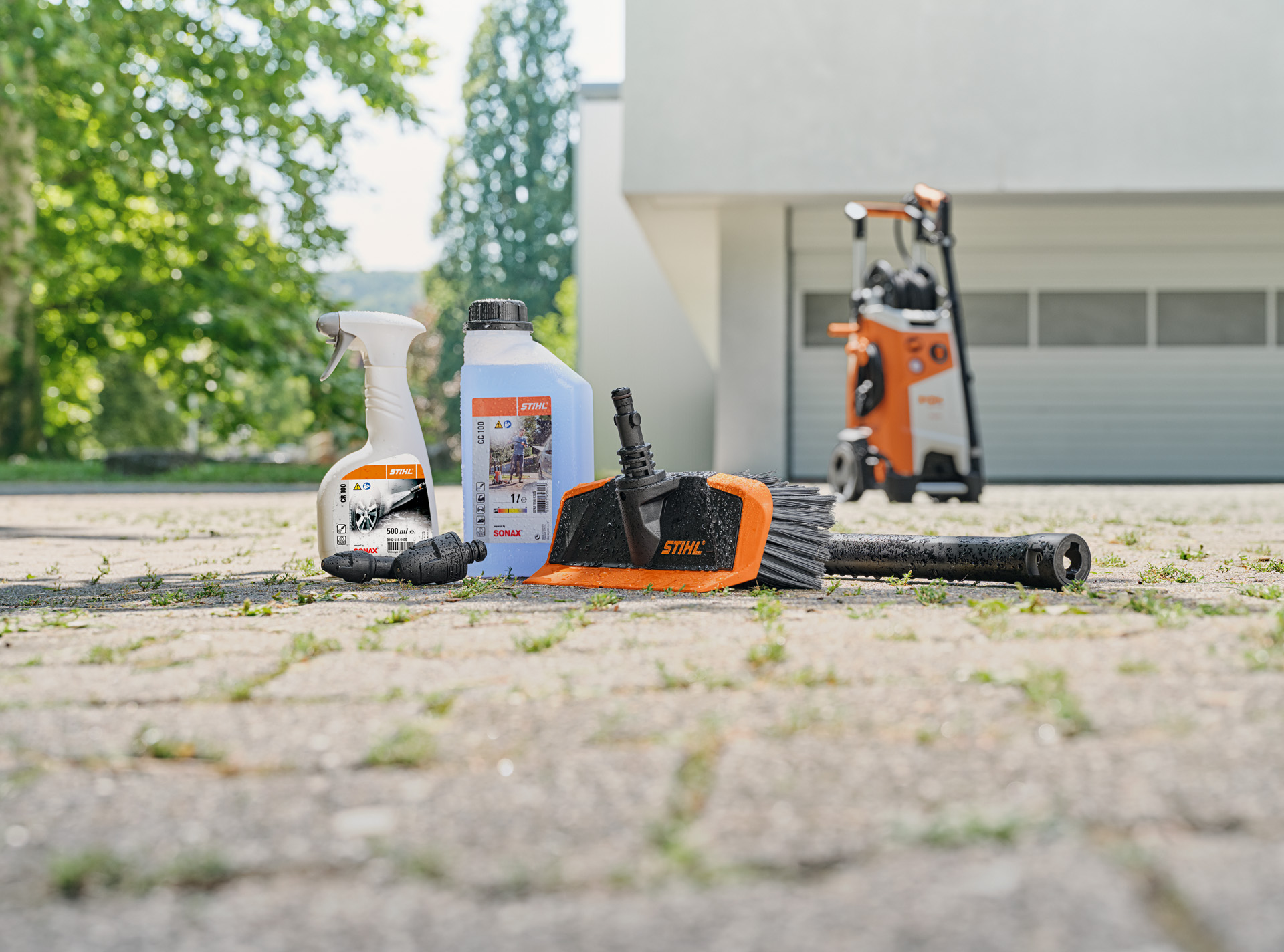 STIHL wheel cleaner, vehicle shampoo and brush on the ground in front of a white garage and a STIHL high-pressure washer