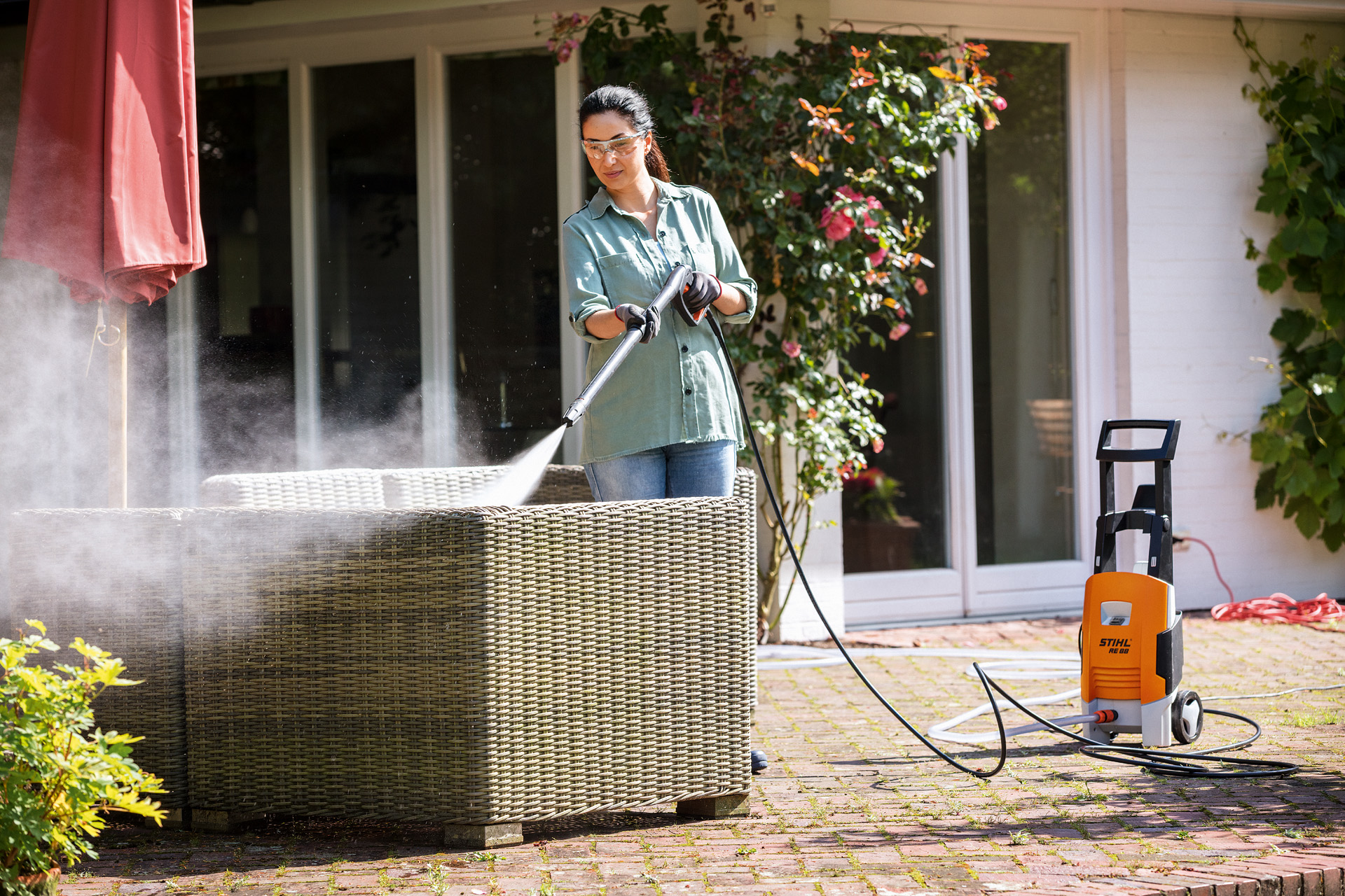 Woman with protective goggles is cleaning her garden furniture on the terrace with the STIHL RE 88 high-pressure cleaner