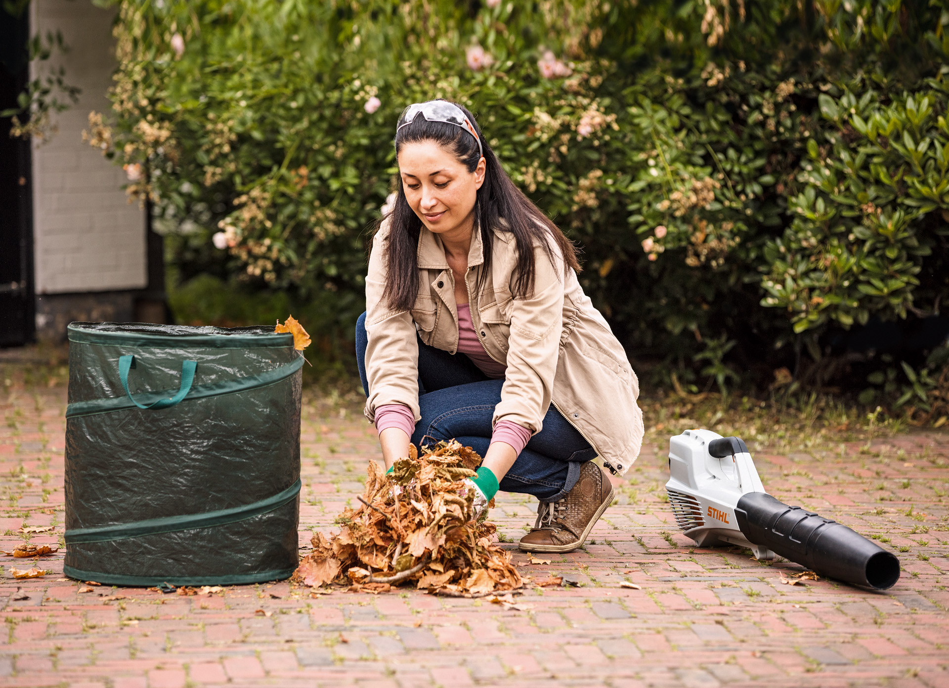 A woman putting leaves into a leaf sack with a STIHL BGA 56 leaf blower on the ground beside her