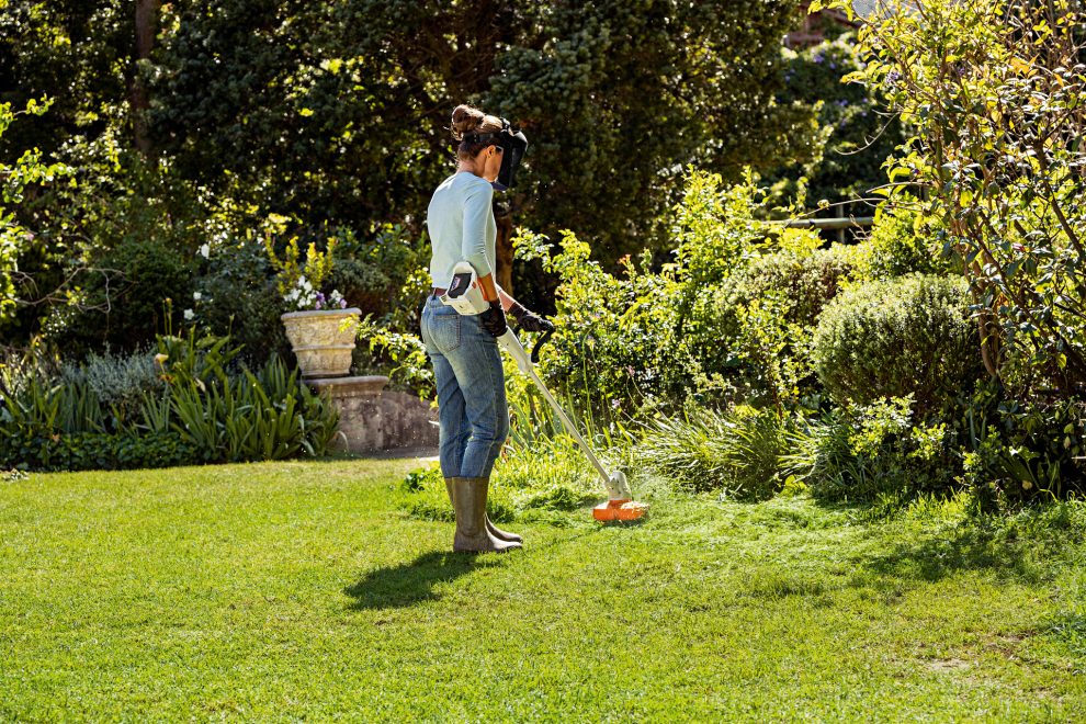 Woman trims tall grass with a STIHL FSA 57 cordless trimmer in a garden