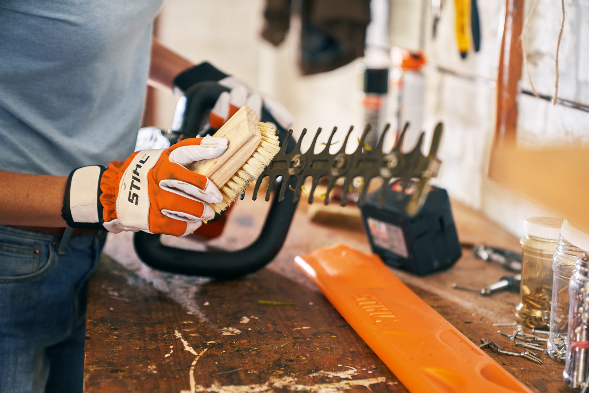 A STIHL HSA 56 cordless hedge trimmer being cleaned with a brush by someone wearing gloves