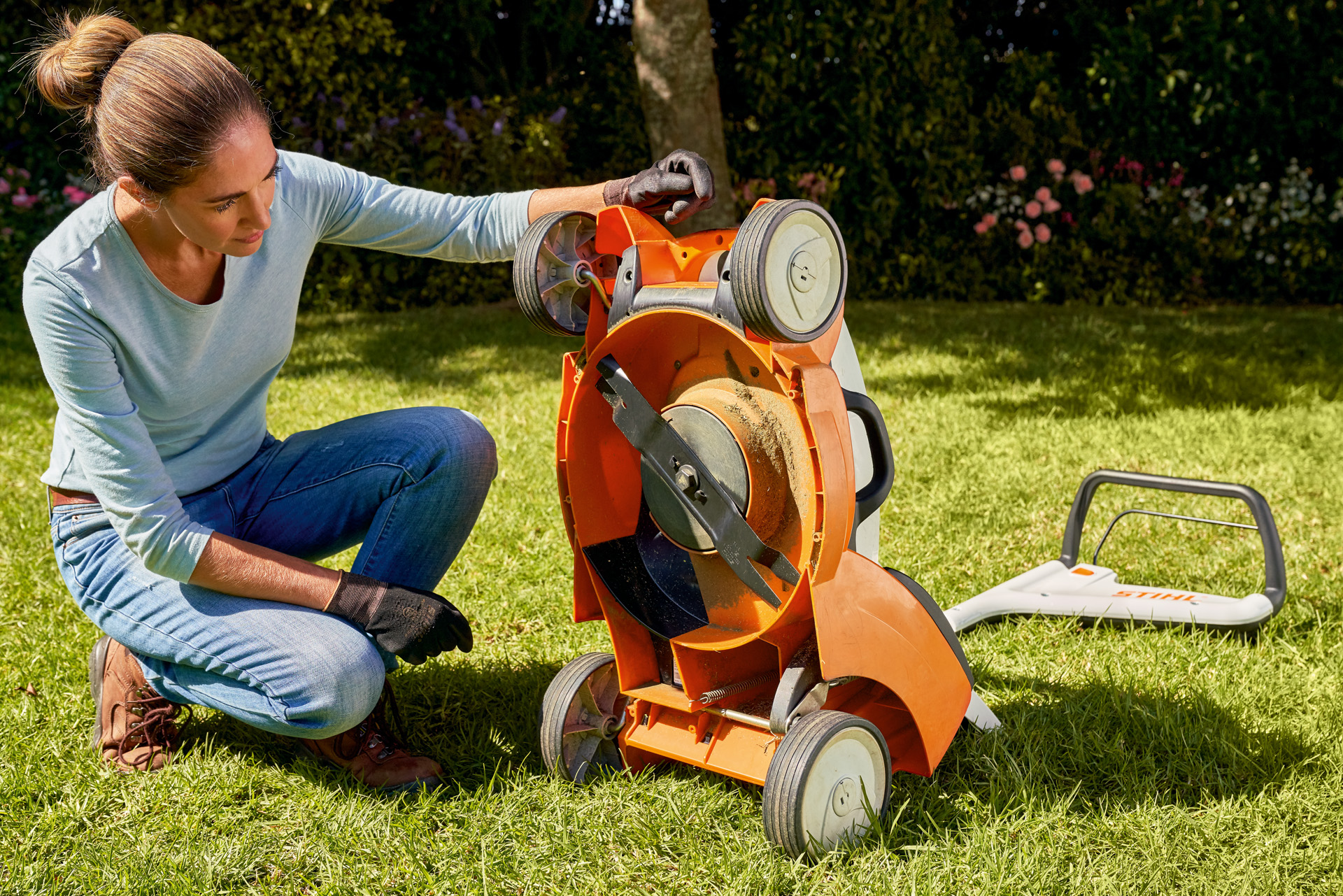 A woman looking at the underside of a STIHL RMA 339C cordless lawn mower