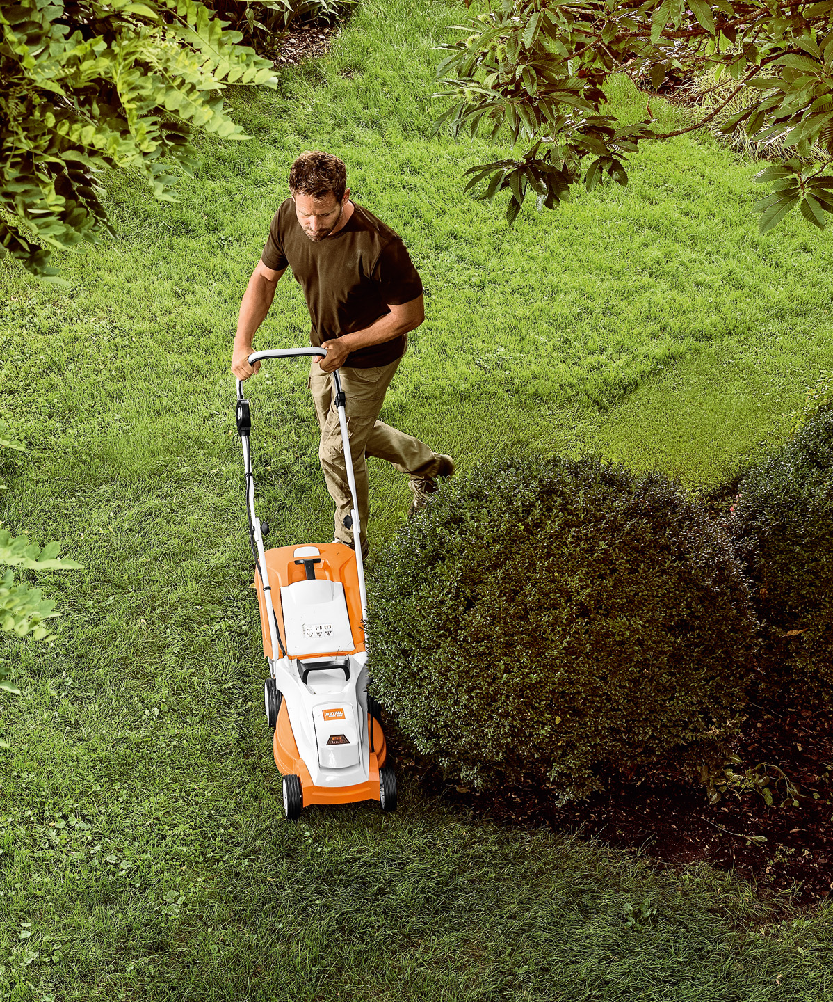 View from above: Man mowing a lawn around a small tree with the STIHL RMA 235 cordless lawn mower.