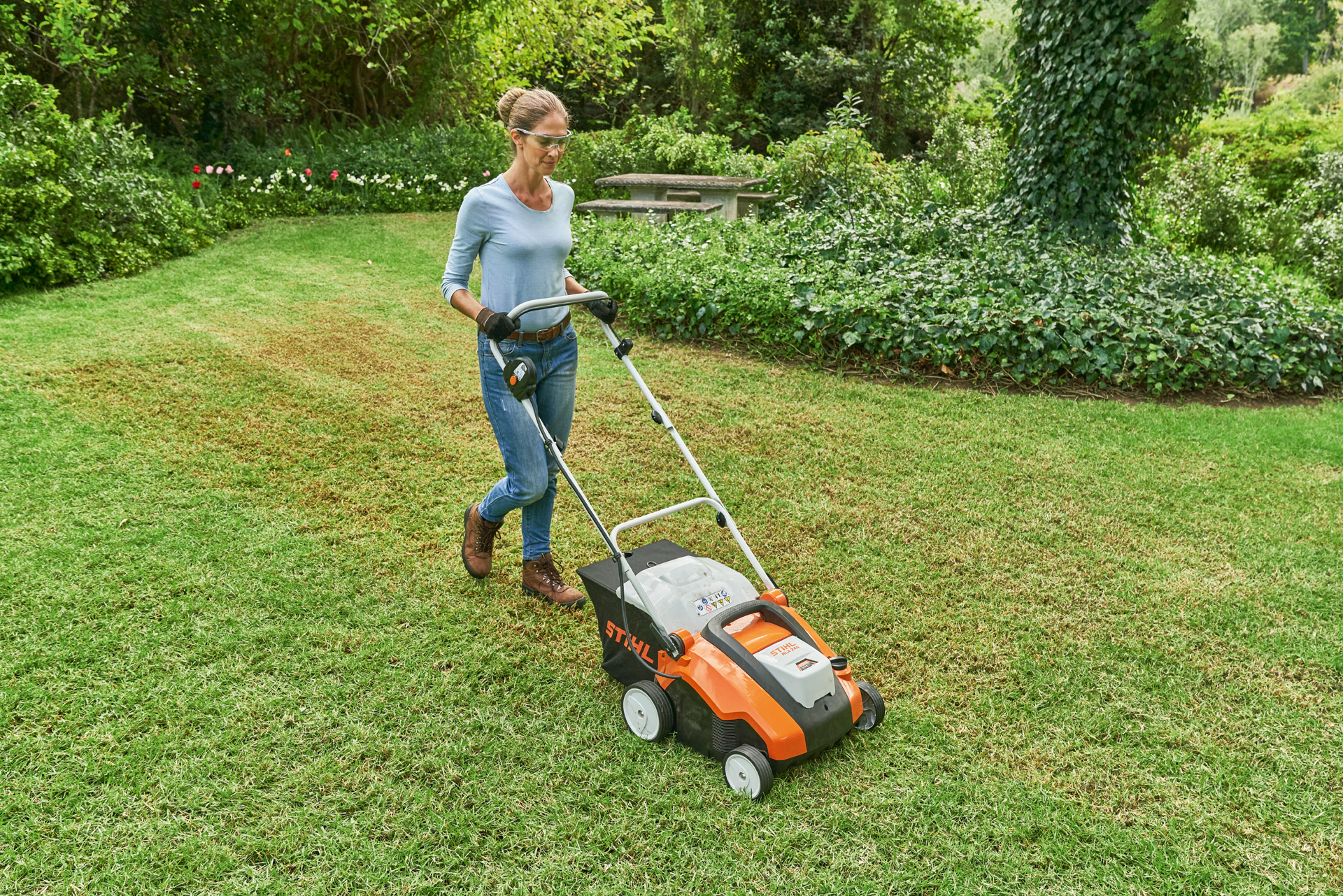 Woman wearing safety glasses and work gloves scarifying a small lawn with the STIHL RLA 240 cordless lawn scarifier.
