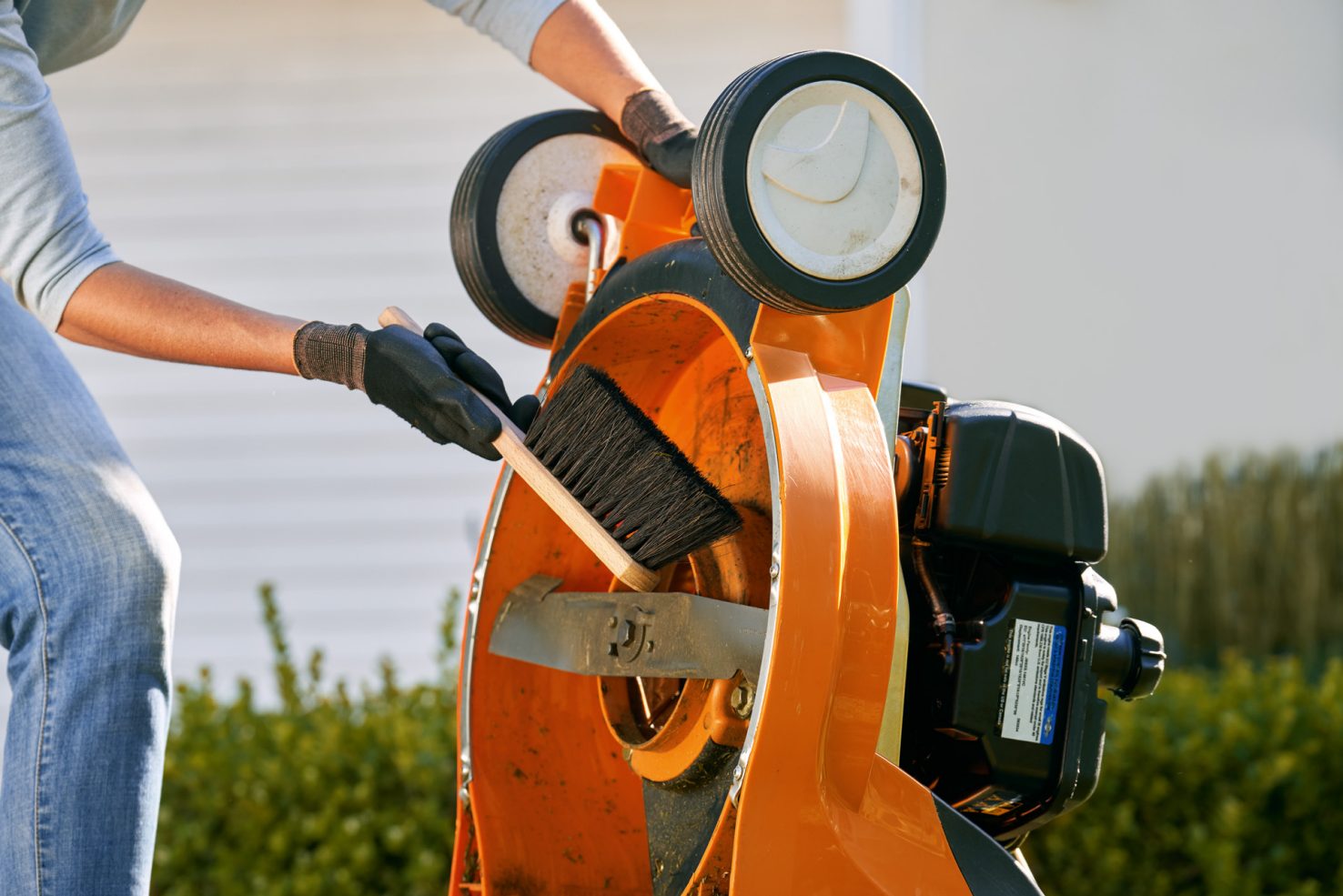 Cleaning the underside of a lawn mower with a brush and gloves