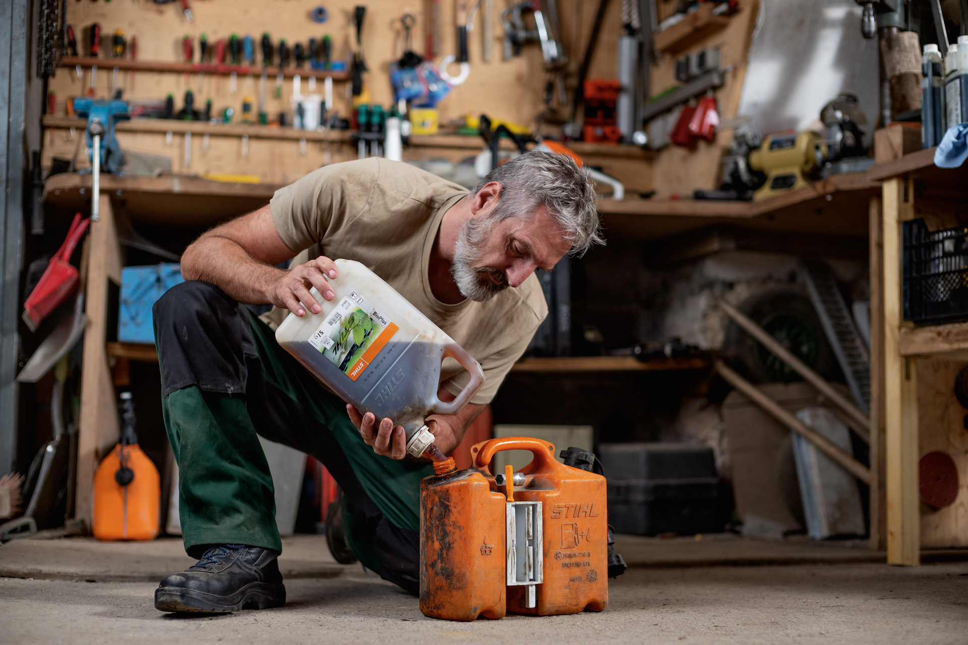 Man kneeling on the floor and filling STIHL fuel into an orange canister