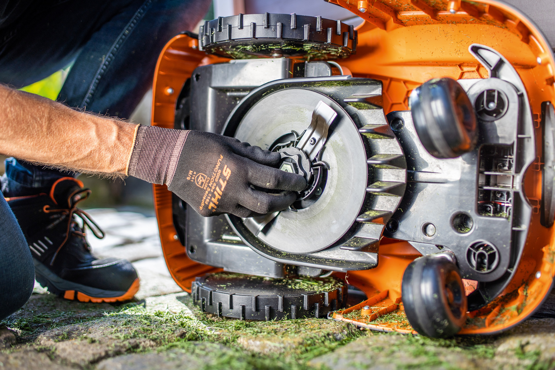 A view of the clean underside of a STIHL iMOW® robot mower, as someone  wearing gloves checks the blade