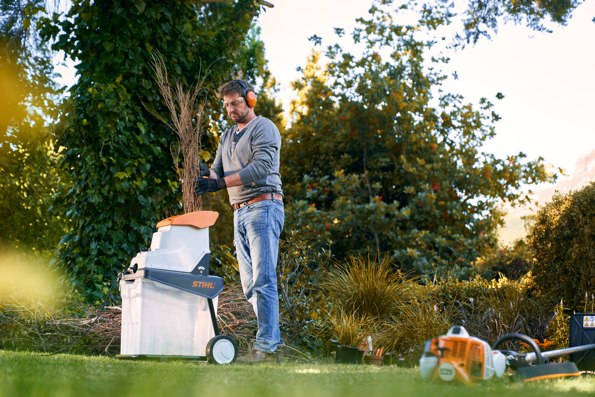 A man wearing ear protection using a STIHL GHE 140 electric shredder in a garden