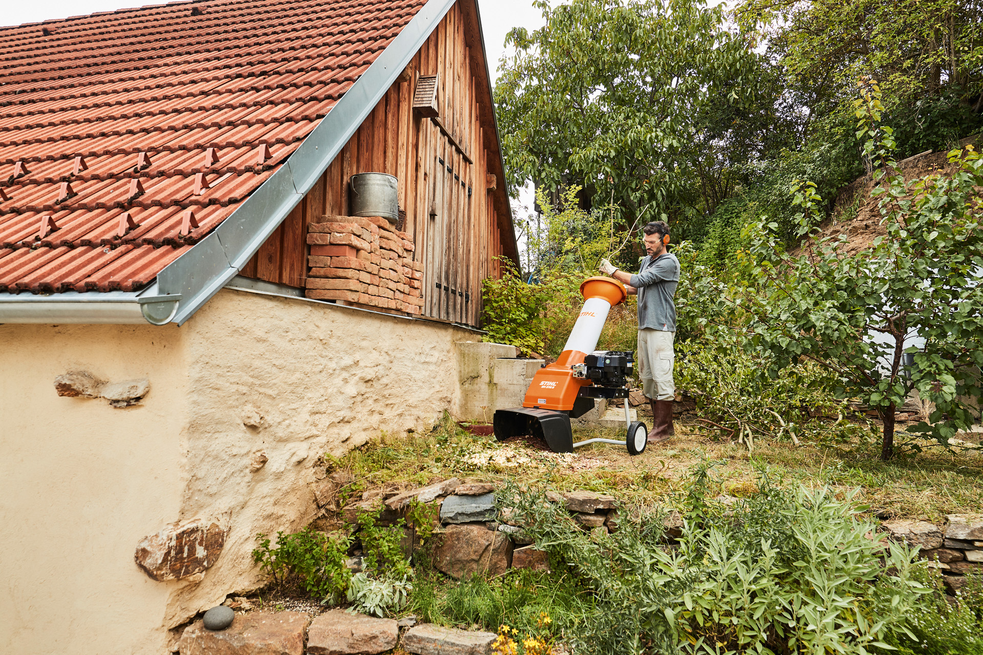 A man using a STIHL GH 370 S petrol shredder on a piece of land beside a house