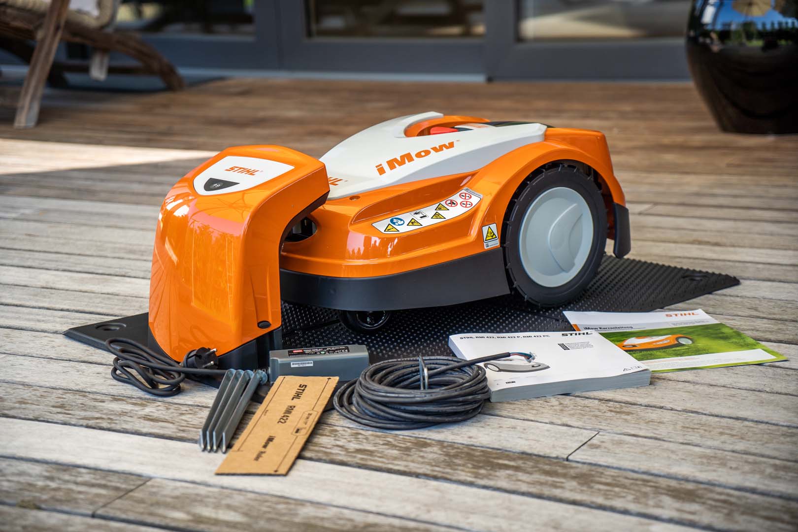 A STIHL iMOW® 422 robot mower on decking with cable and operating instructions