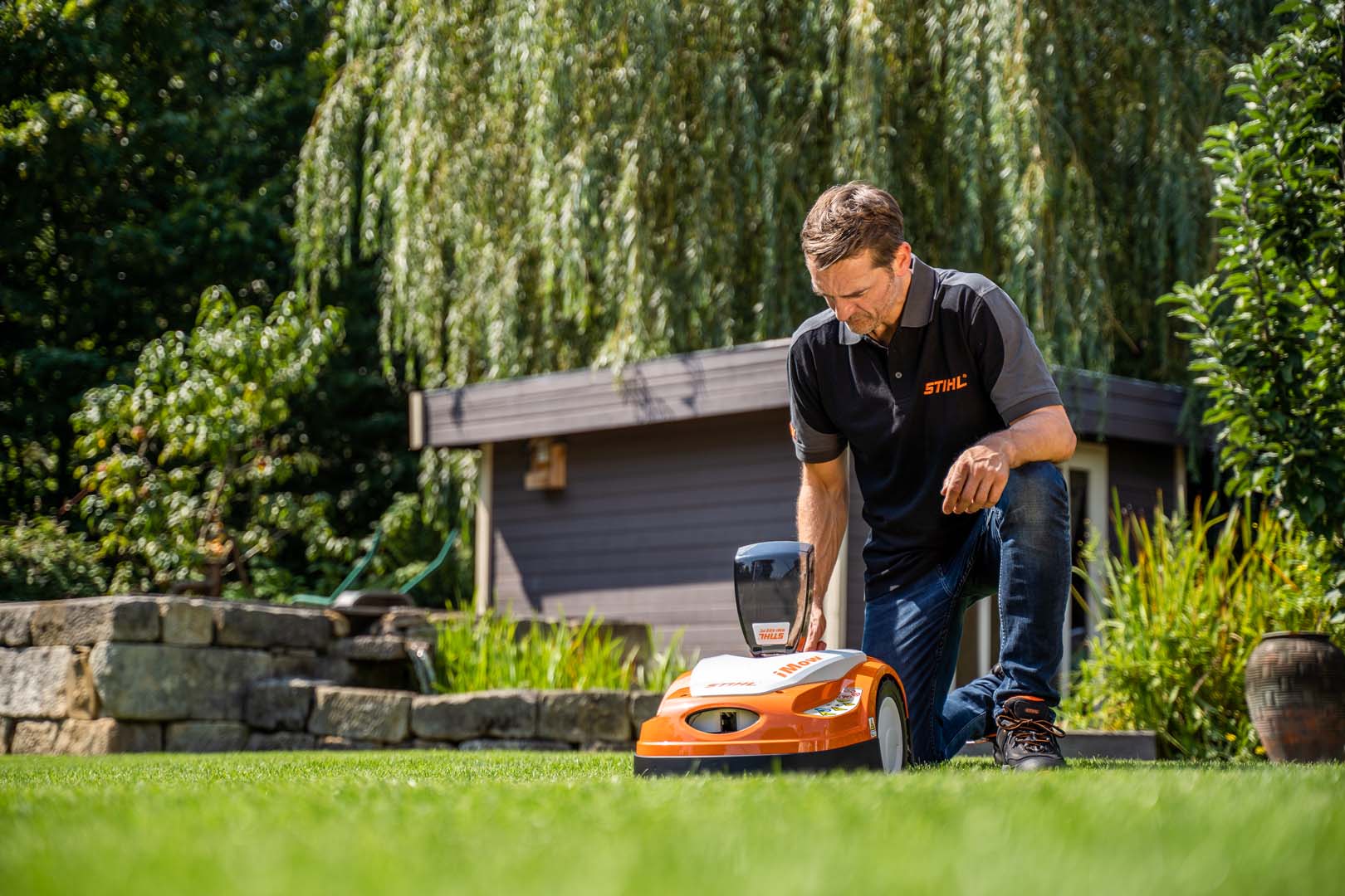 A STIHL dealer kneeling to adjust settings on a STIHL RMI 422 iMOW® robot mower in a garden