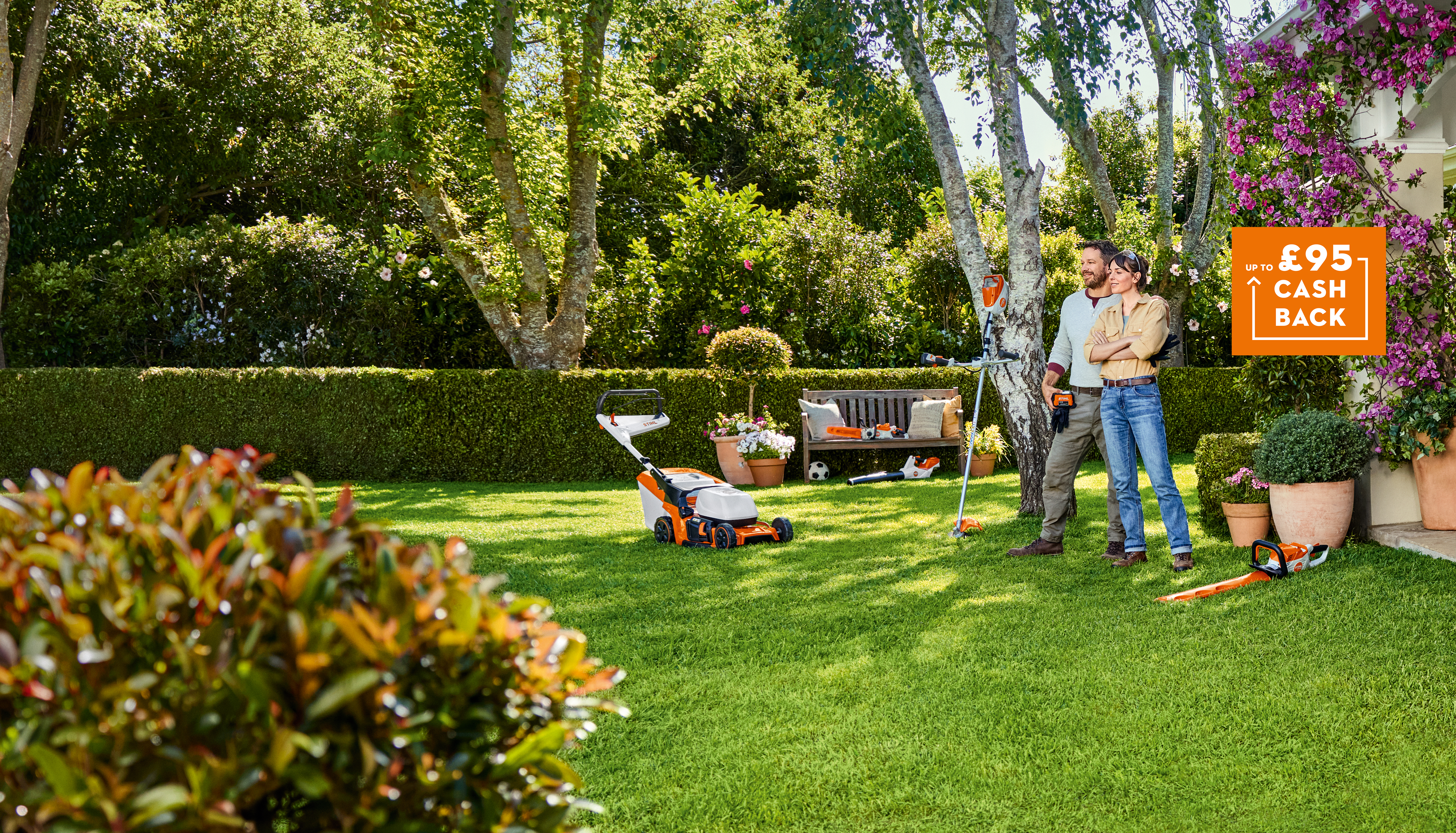 Up to £95 cashback square orange badge on image of couple in lush well-maintained garden surrounded by STIHL AK System tools like a brushcutter, hedge trimmer, lawnmower, chainsaw and blower