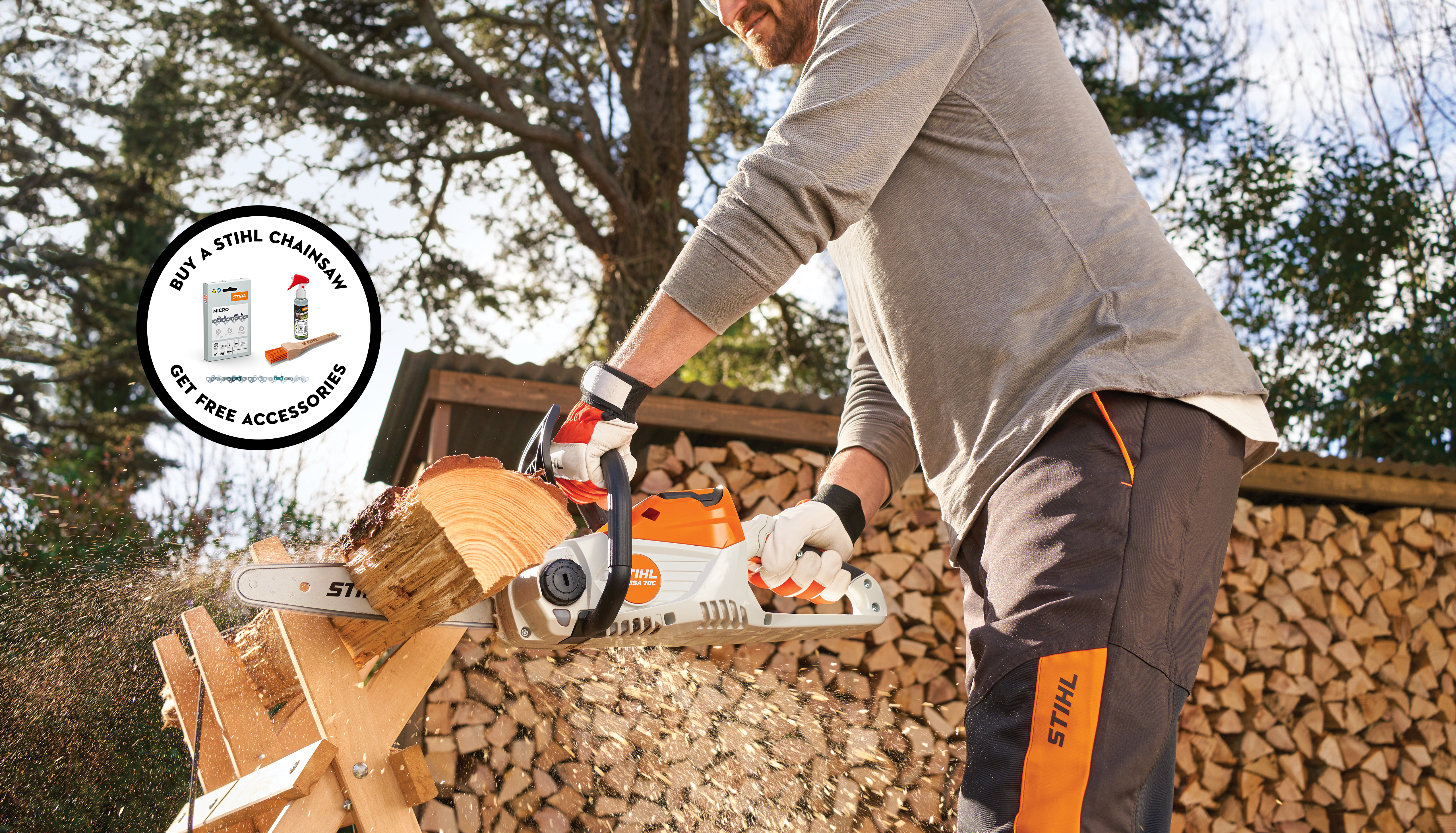 man cutting firewood with STIHL MSA 70 chainsaw on sawhorse in garden