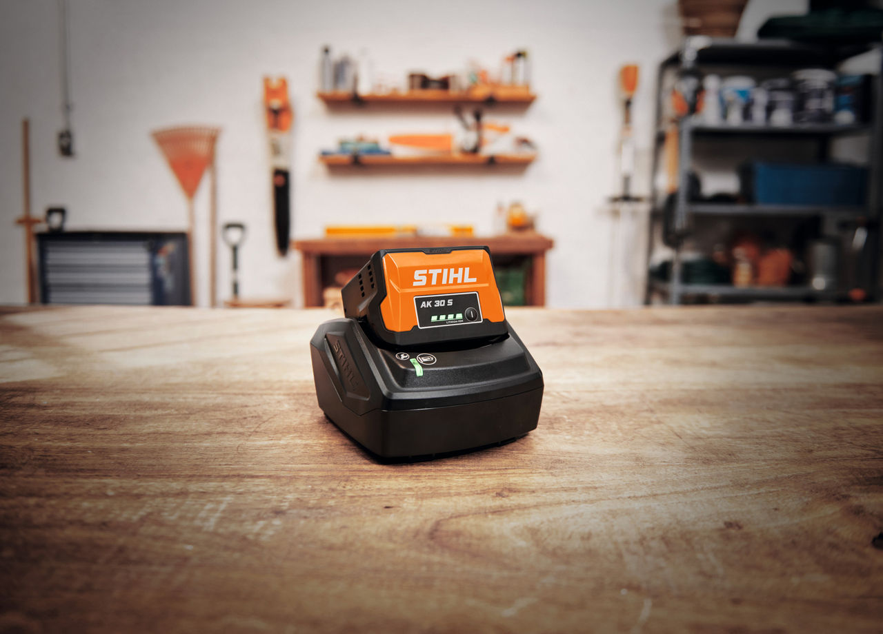 An AK battery with STIHL battery technology is charging on a bench in a workshop