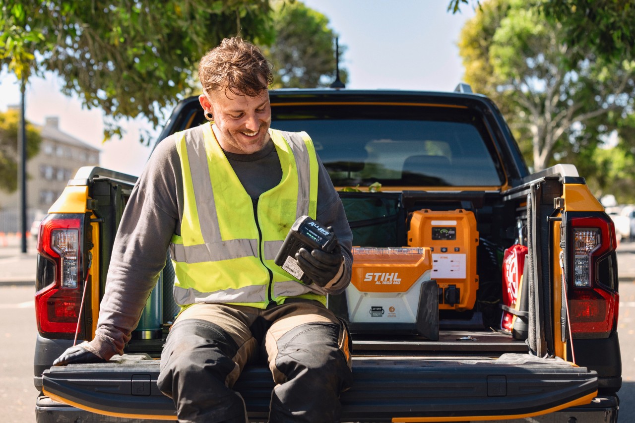 A working man holding an ALLPRO battery on a truck