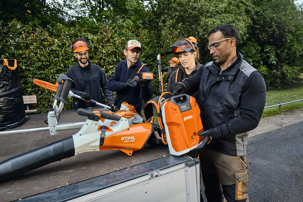 A team of landscaping professionals unloads their STIHL professional battery-powered equipment from the loading area of a vehicle.